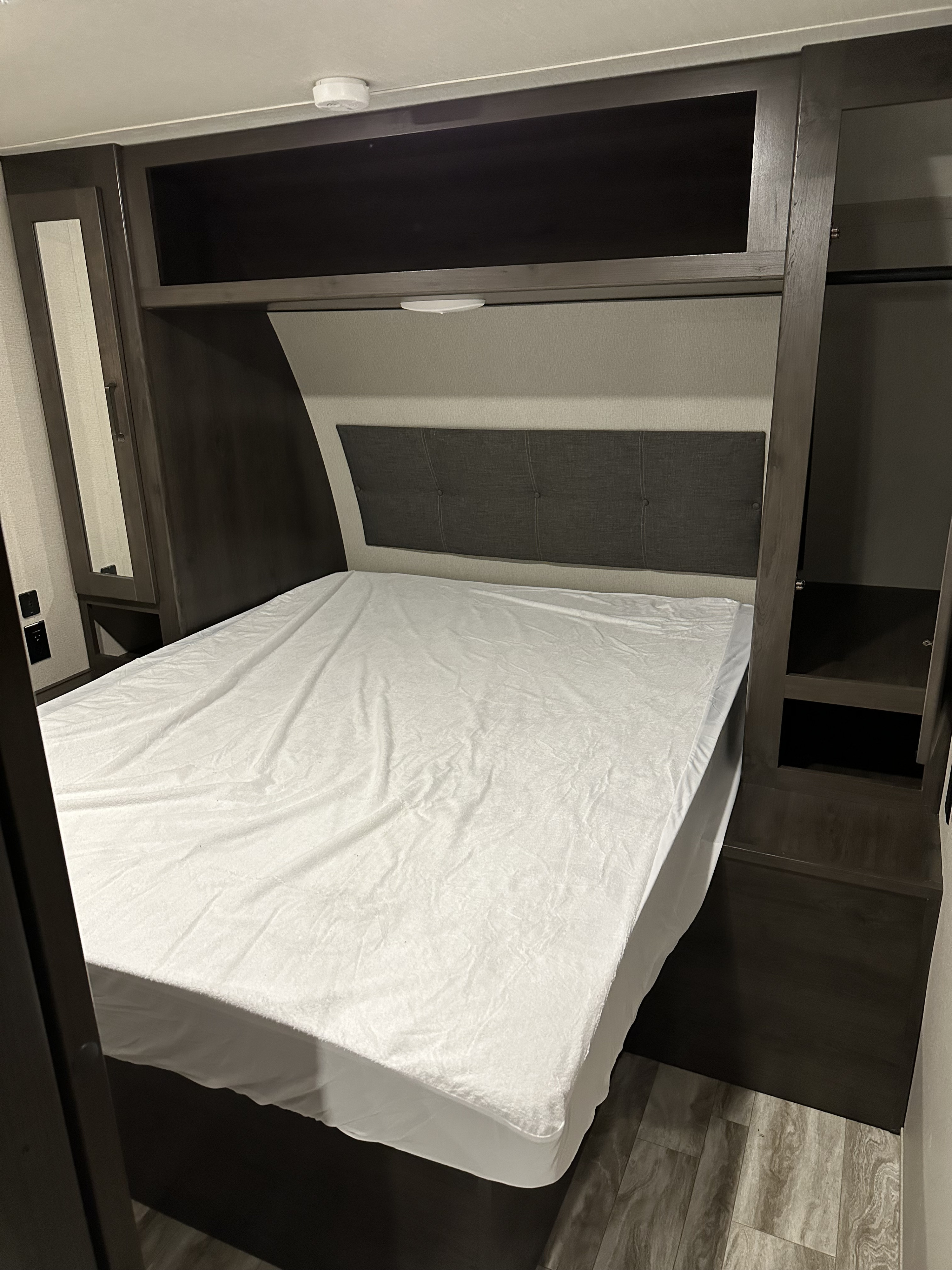 Cozy RV rental bedroom featuring a white-sheeted bed, gray headboard, and dark wood cabinetry with storage.. Grand Design Transcend Xplor 2022