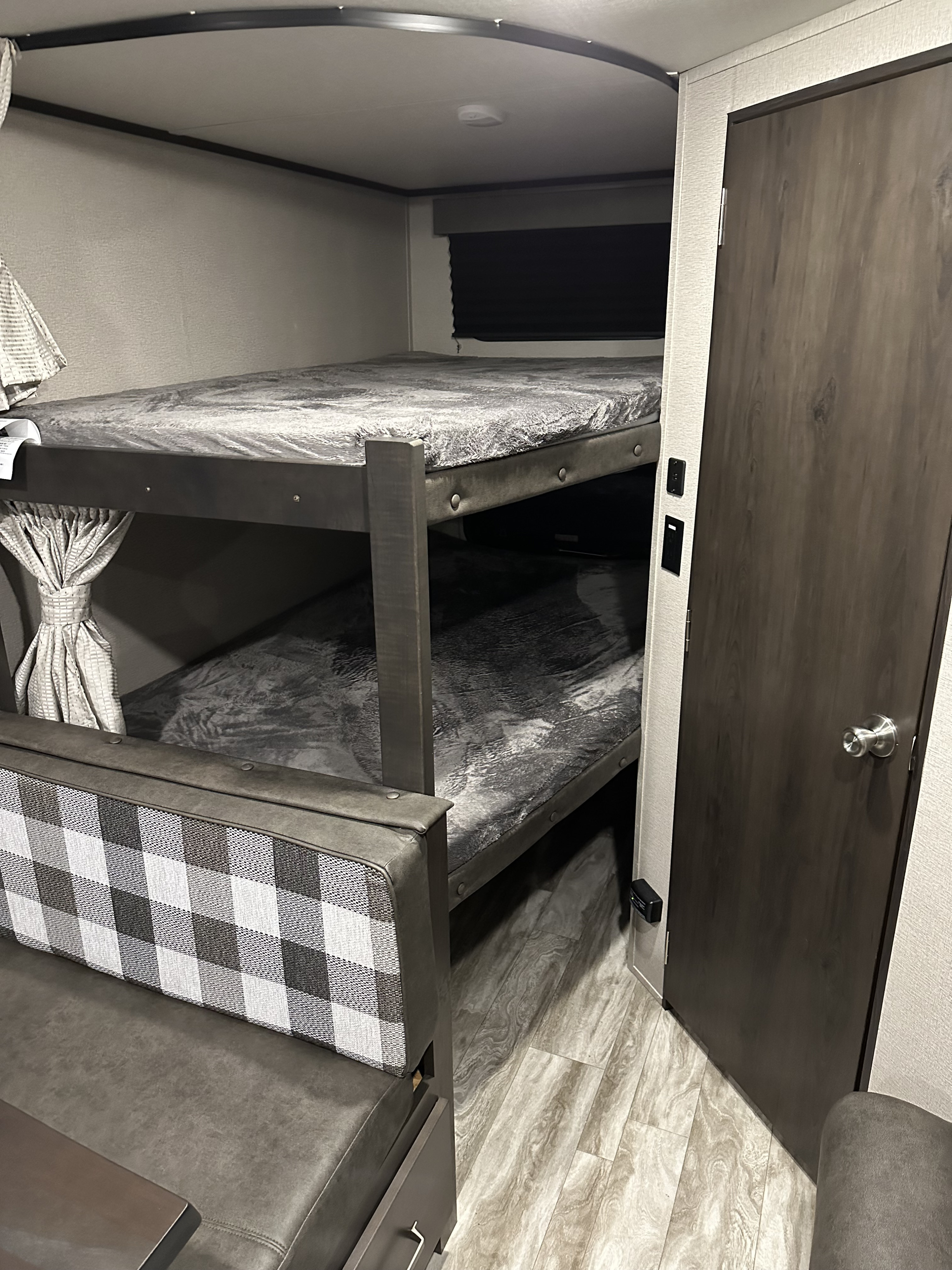 RV rental interior: bunk beds with plastic-covered mattresses, plaid dinette, and a wood-paneled door.. Grand Design Transcend Xplor 2022