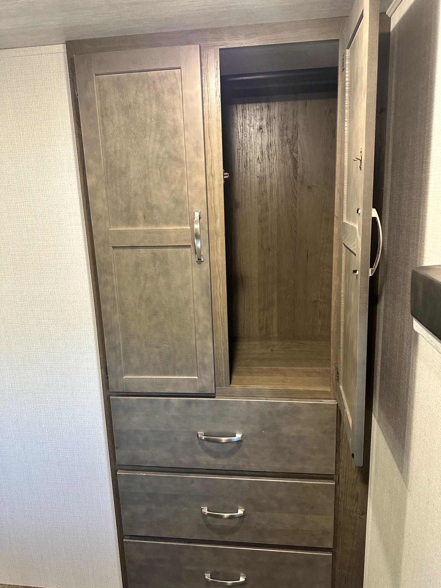 Wooden wardrobe in an rv rental, featuring an open cabinet with a hanging bar and three bottom drawers for efficient storage.. Keystone Cougar 2023