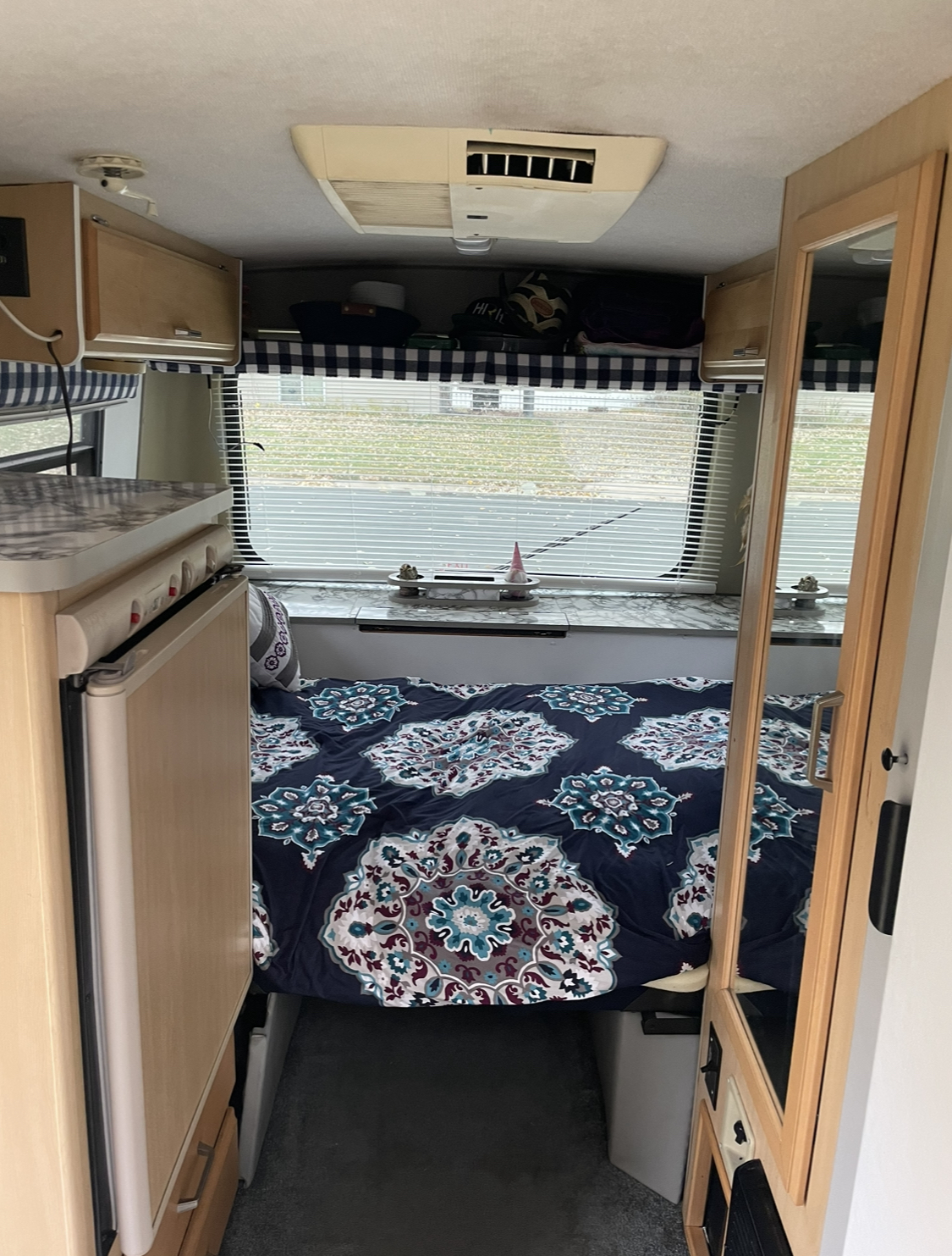 Explore this RV rental's inviting interior: comfy bed with patterned comforter, compact kitchen, and overhead storage.. Other Other 2000