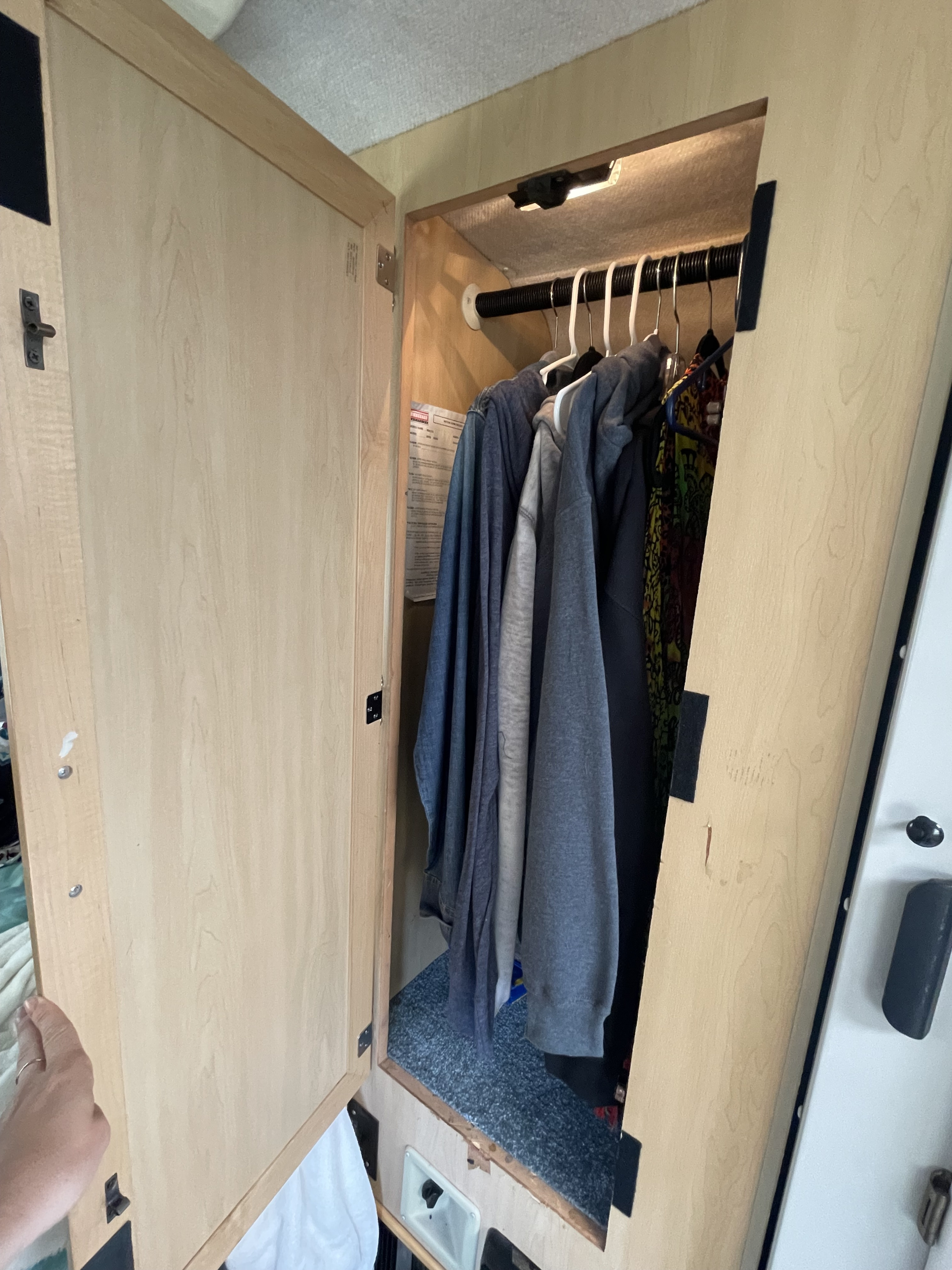 Inside an RV rental, a compact wardrobe holds hanging clothes, featuring an overhead light and carpeted floor for efficient storage.. Other Other 2000