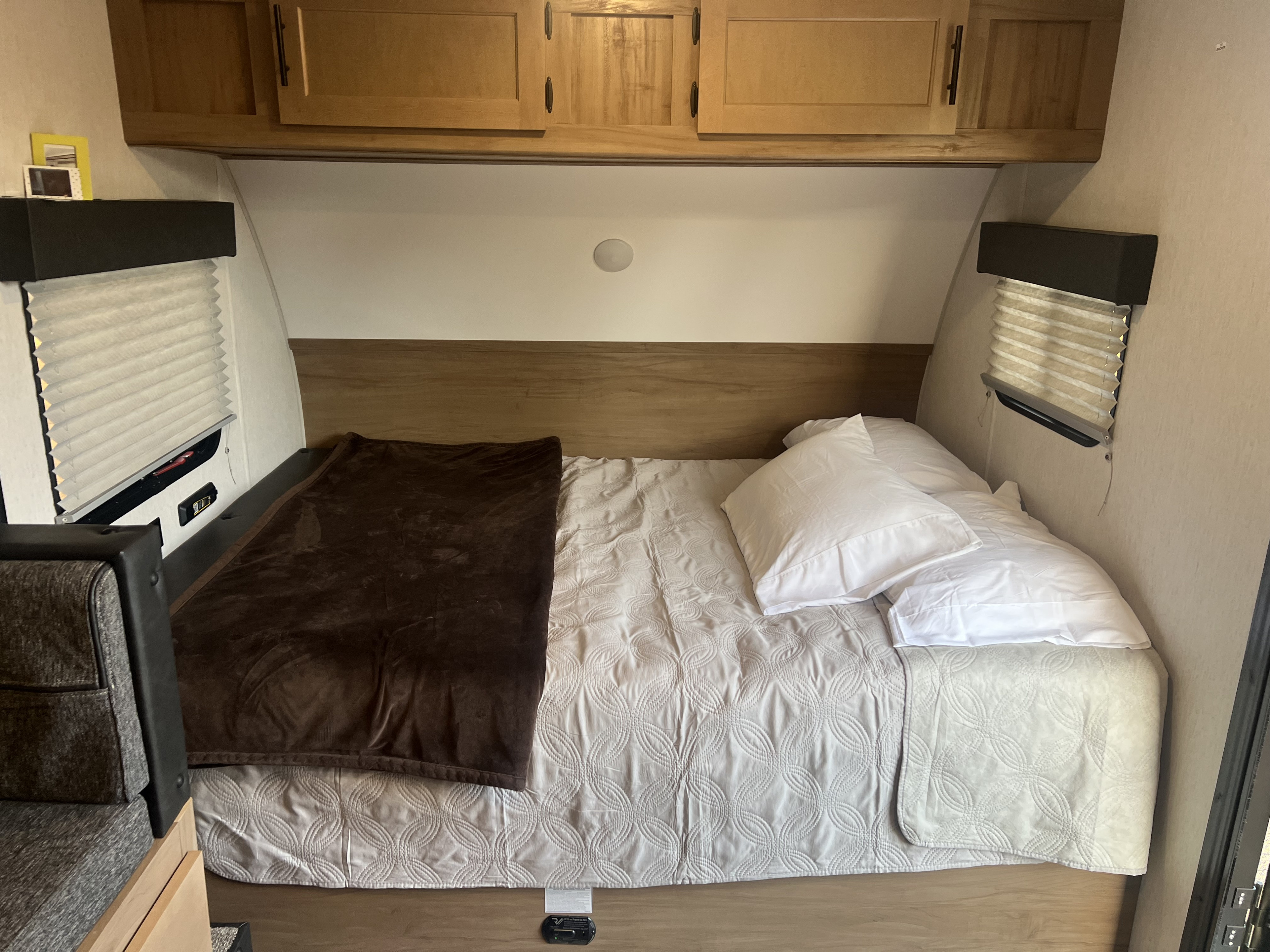 RV rental bedroom featuring a comfy bed with white pillows, quilted comforter, wood cabinets, and window blinds.. Forest River Wolf Pup 17JG 2023
