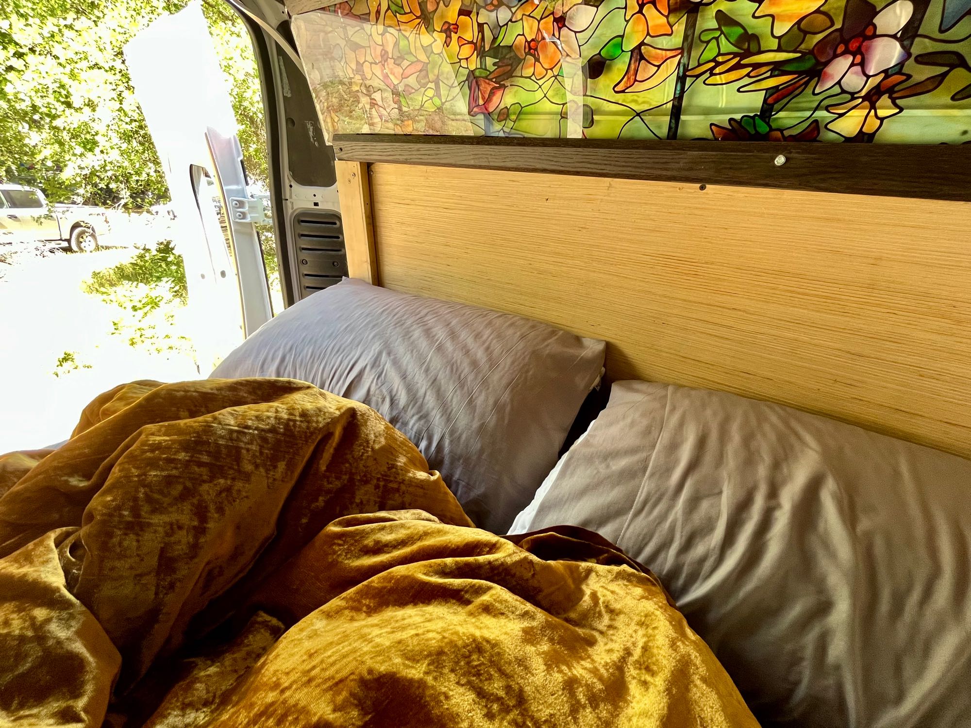 Cozy RV rental bed with gold blanket, gray pillows, stained glass & open door view.. Dodge Other 2018