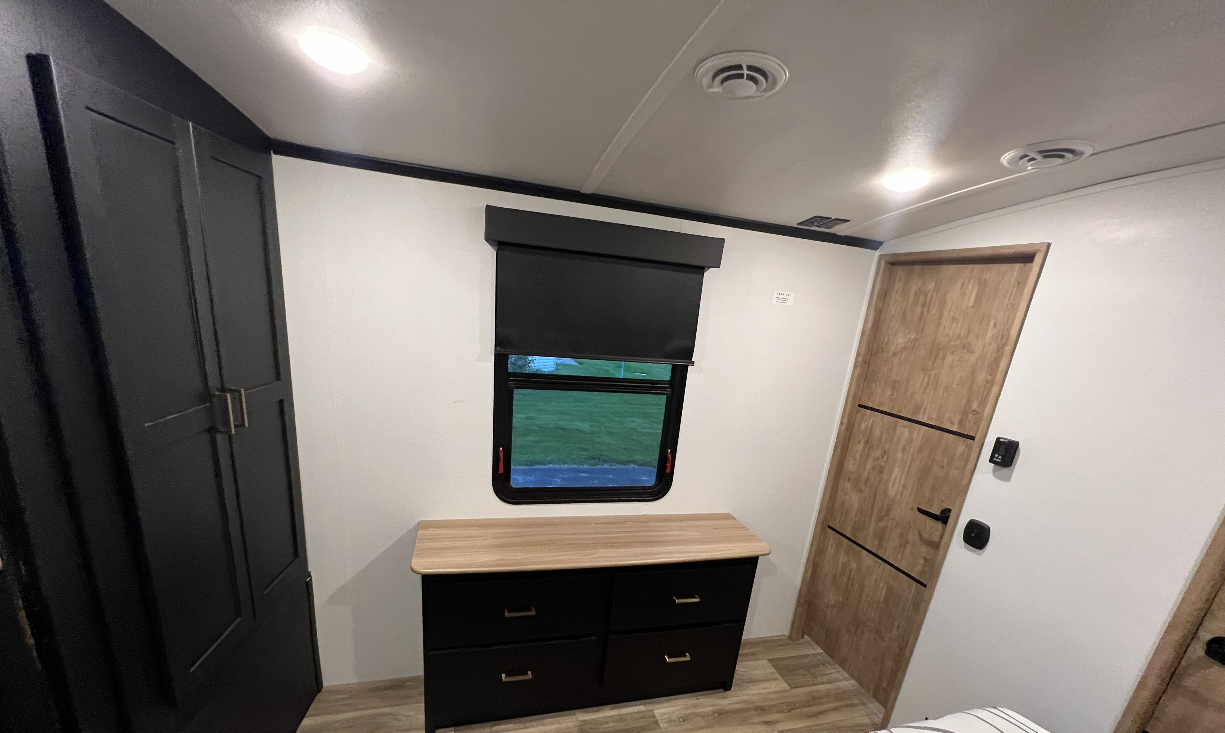 Step inside this RV rental's modern bedroom: dark wardrobe, light wood dresser, and window with blind.. Keystone RV Outback 2022