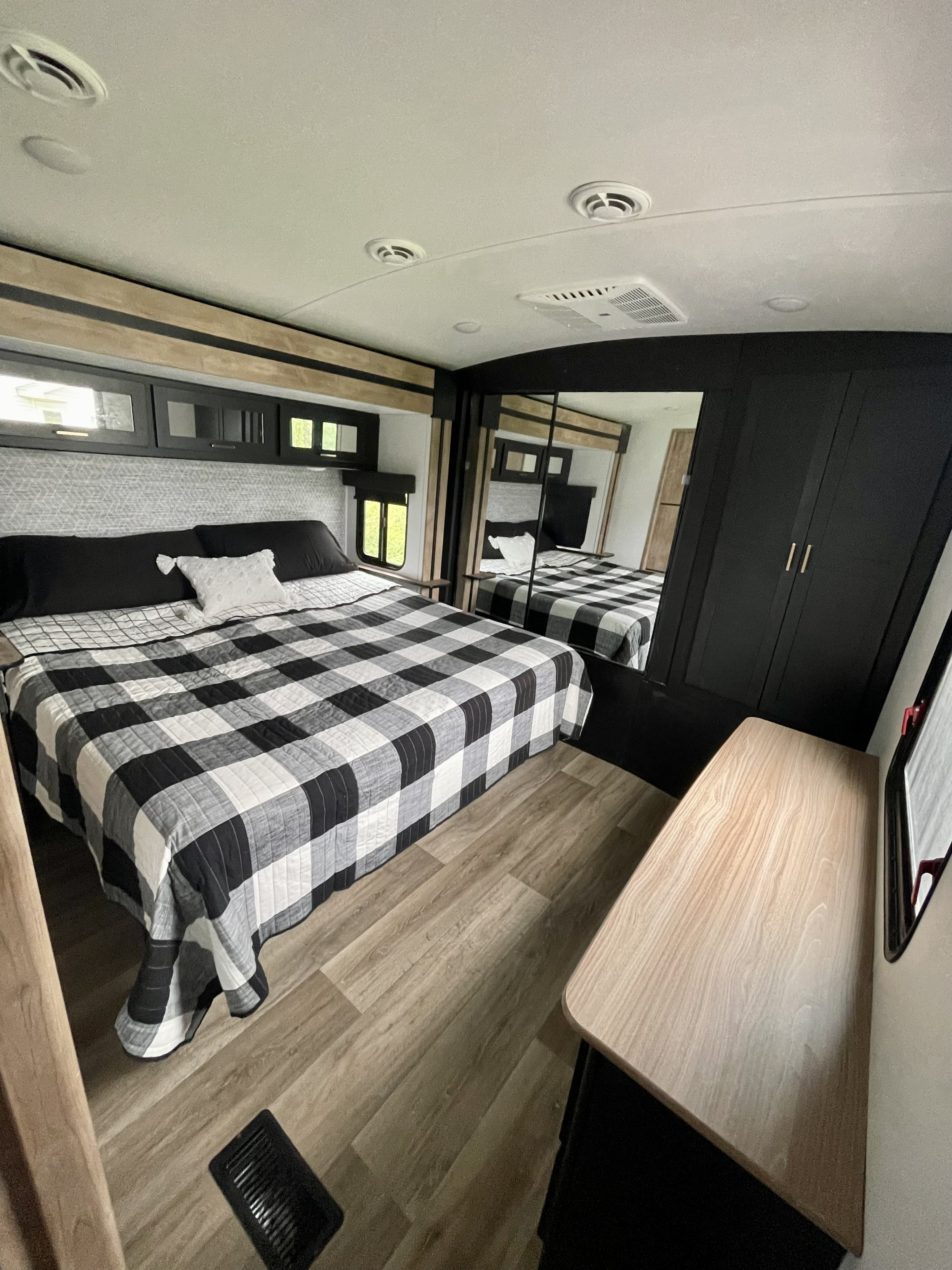 Spacious RV rental bedroom with buffalo check bedding, overhead cabinets, a mirrored wardrobe, and light wood floors.. Keystone RV Outback 2022
