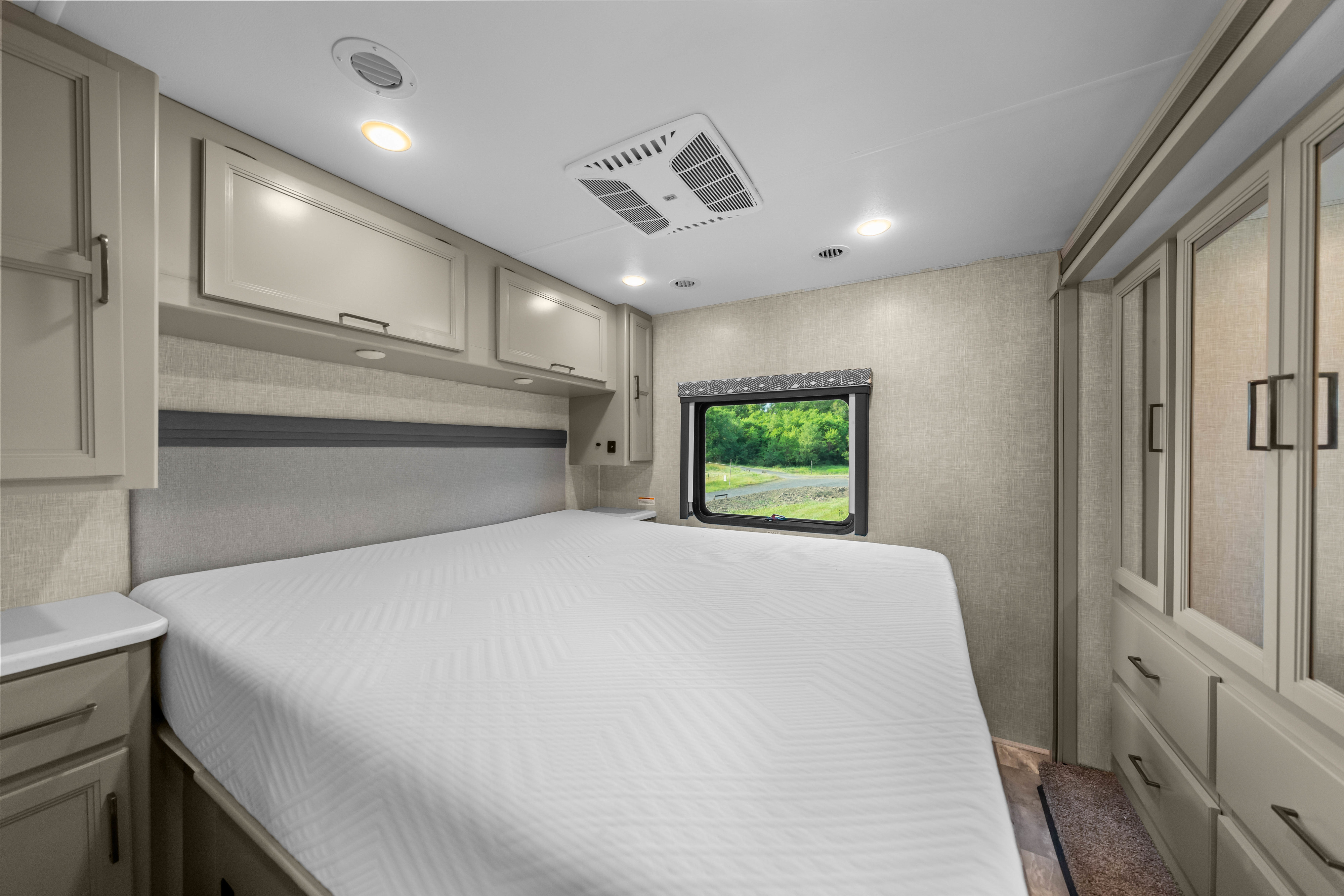 Modern RV rental bedroom: cozy bed, overhead cabinets, window with view, and built-in wardrobe.. Thor Windsport 2023