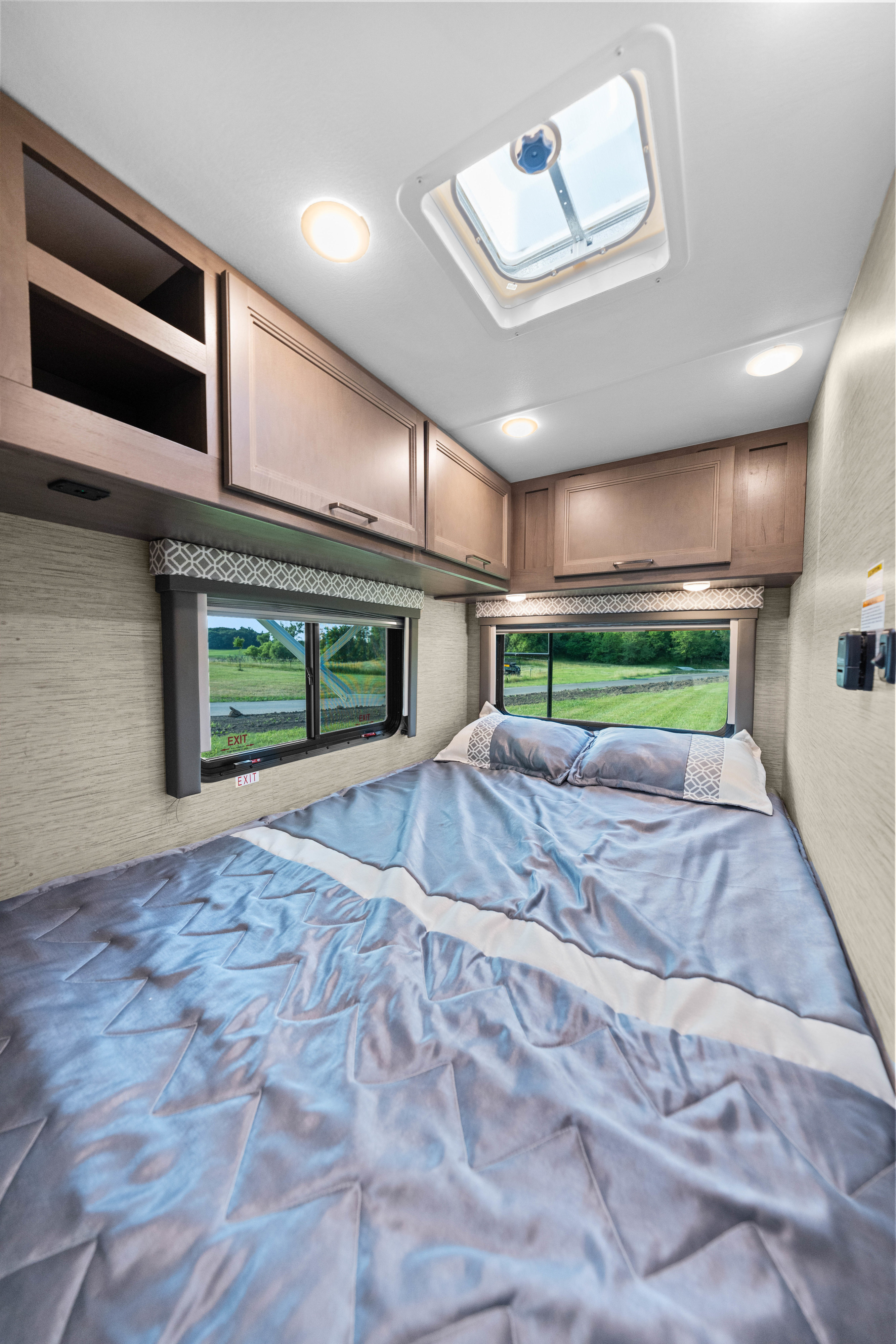 Cozy RV rental bedroom featuring a spacious bed, ample storage cabinets, bright windows, and an overhead skylight.. Thor Coleman 2023