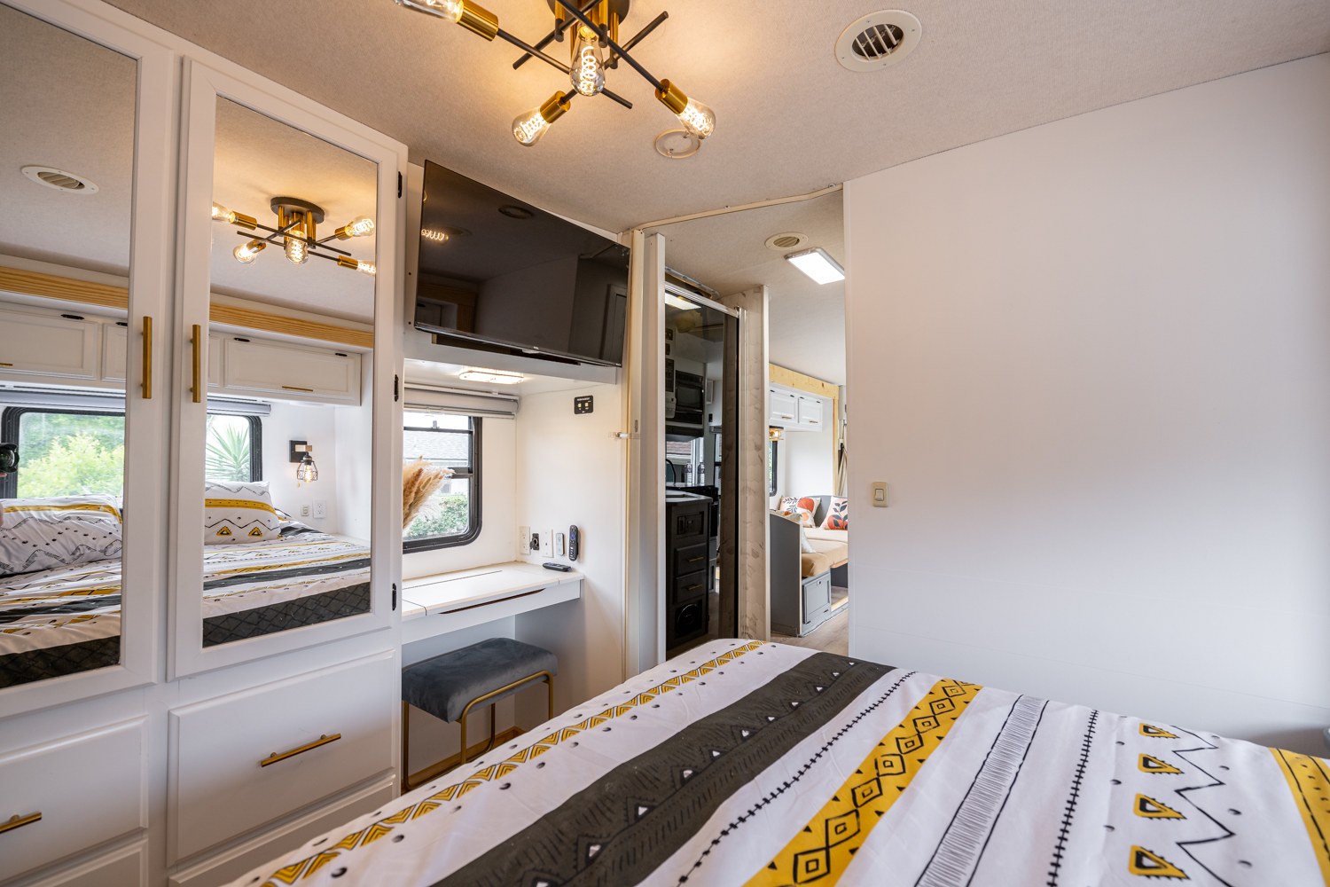 Modern RV rental interior: bedroom with mirrored wardrobe, TV, and desk leading to kitchen/living area.. Winnebago Sightseer 2006