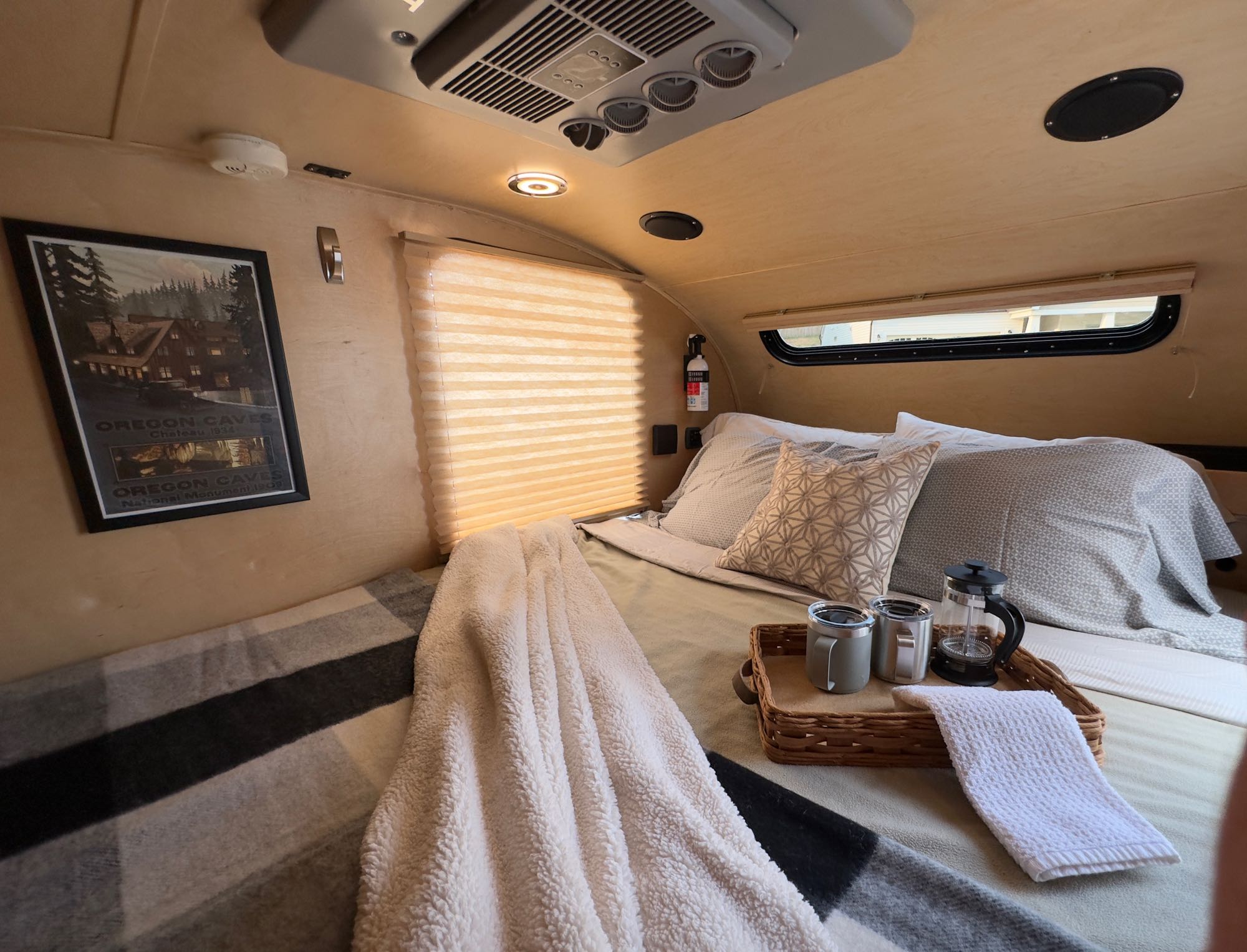 Inside a cozy RV rental: comfy bed, blankets, French press coffee setup, and an Oregon Caves poster on the wall.. Little Guy Little Guy Trailer 2013