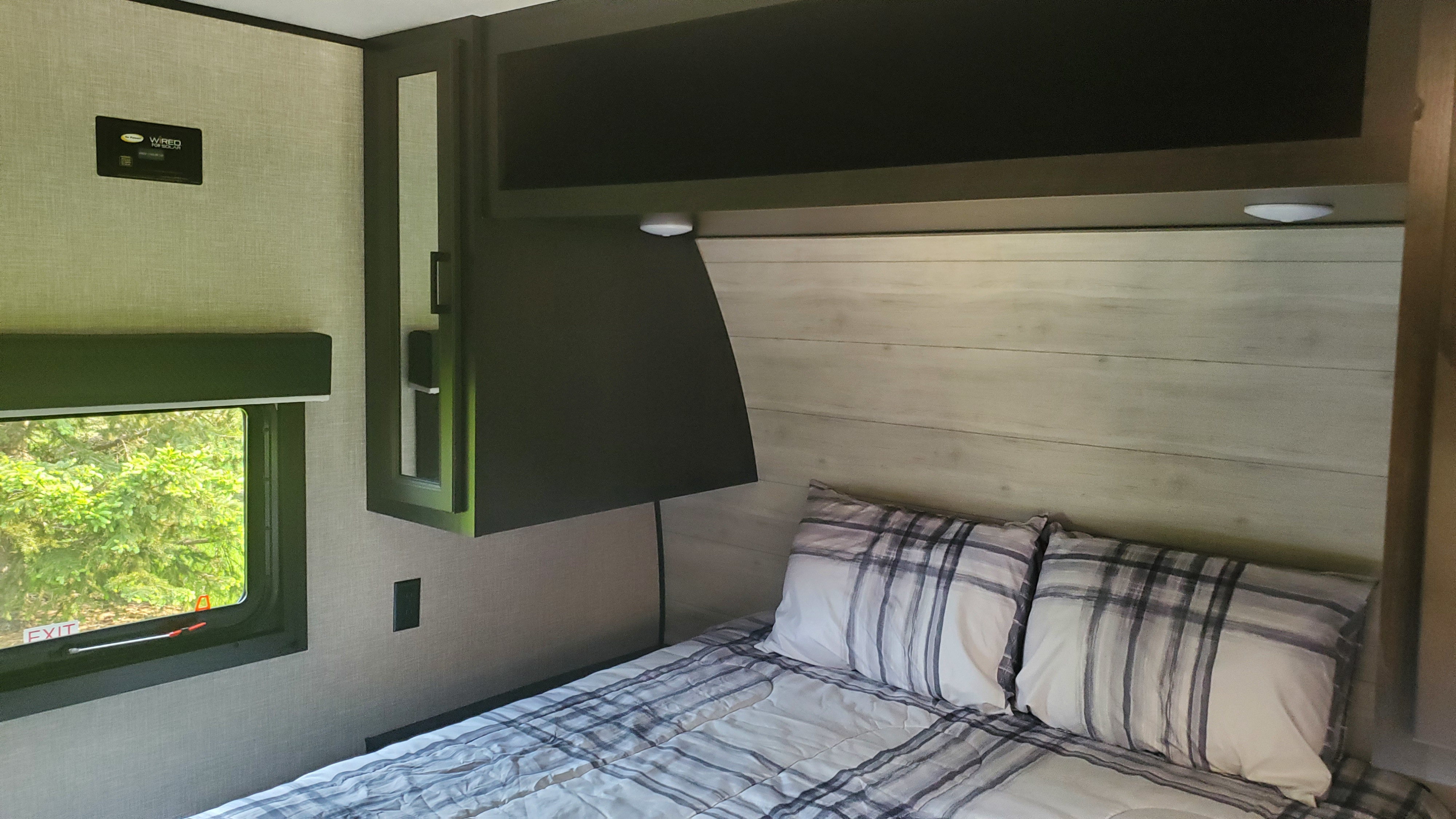 Inviting RV rental bedroom featuring a comfy bed with plaid bedding, window with nature view, and overhead storage.. Jayco Jay Flight 264BH 2023