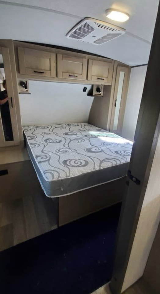 Comfortable RV rental bedroom with a patterned mattress, overhead storage cabinets, and a ceiling AC unit.. Heartland RVs Sundance Ultra Lite 2021