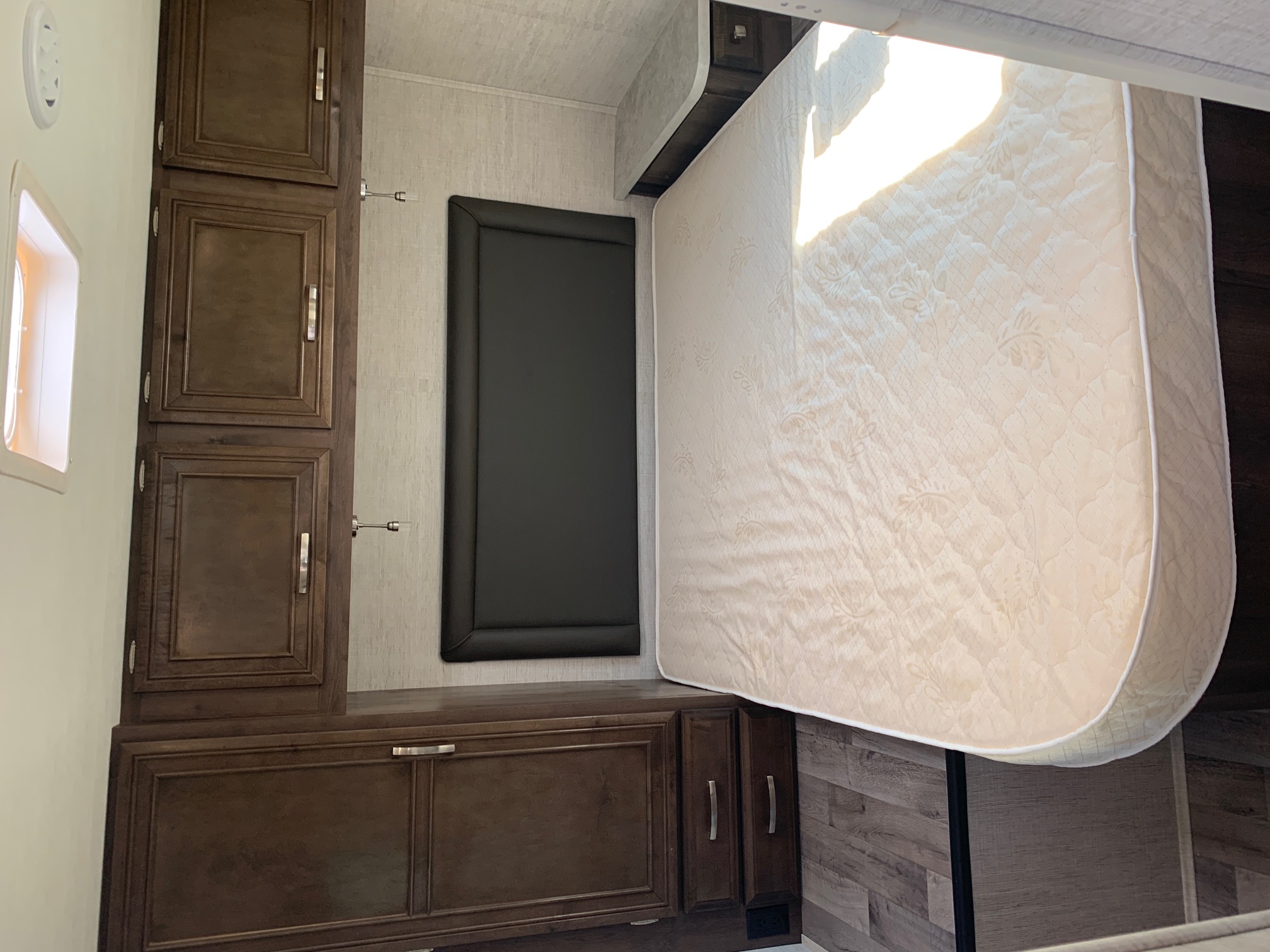 RV rental bedroom with a comfortable mattress, dark headboard, overhead cabinets, side closet, and bright skylight.. Jayco Redhawk 29XK 2023