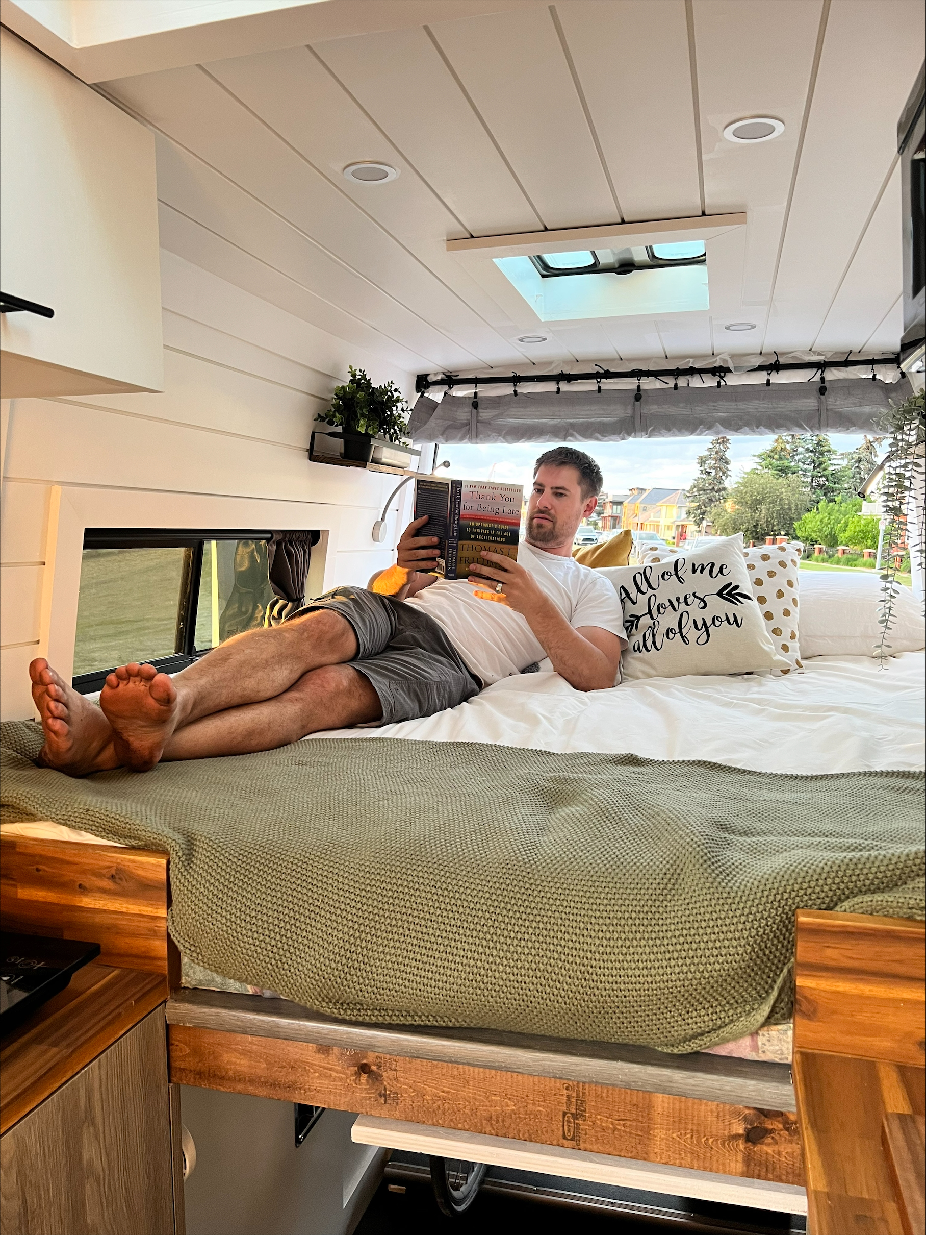 Enjoying a cozy moment in an RV rental! Man reads in a comfortable camper van bed with a scenic view outside.. Mercedes-Benz Sprinter 2012