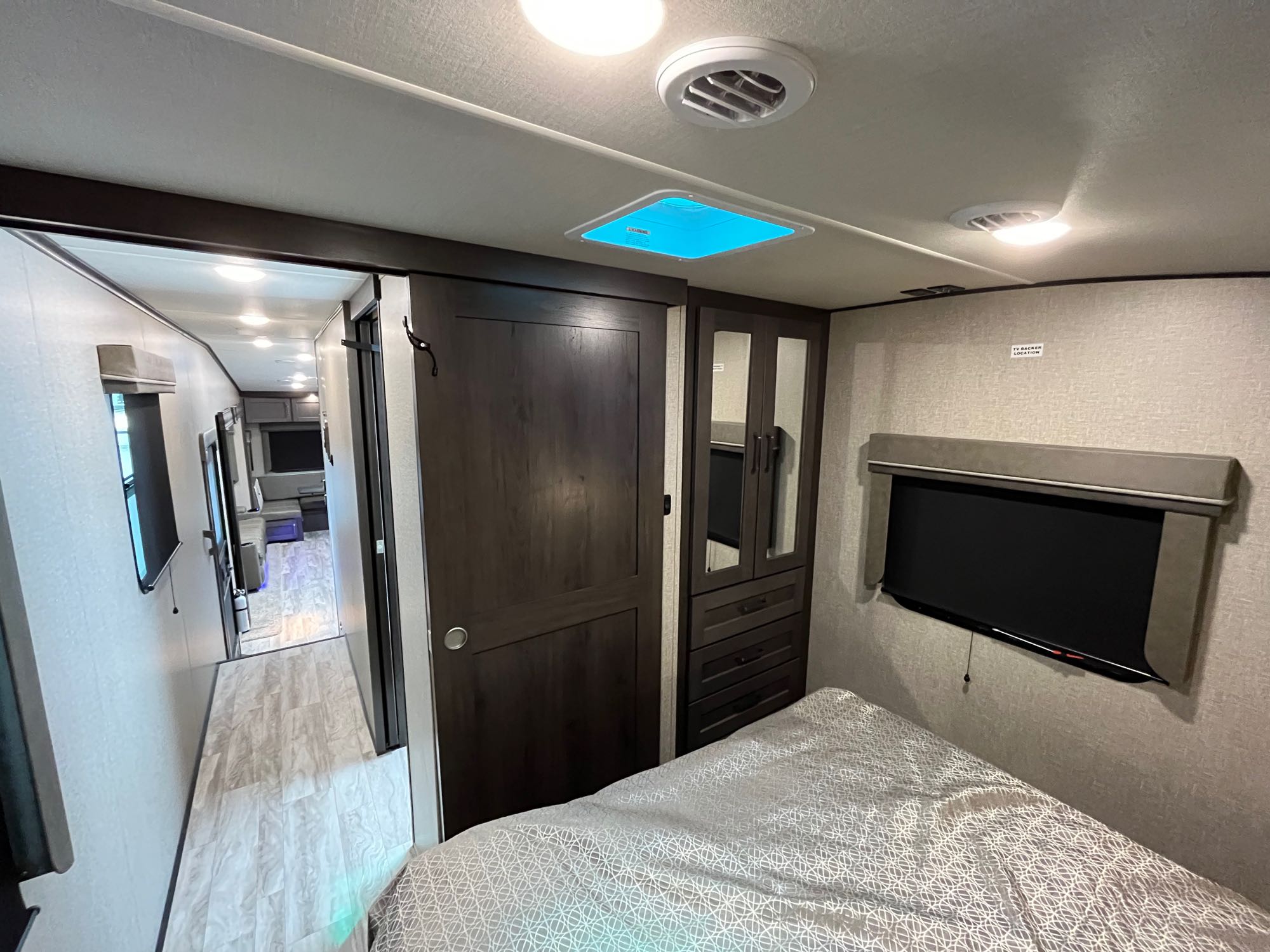 Inside an RV rental, a cozy bedroom with storage and TV connects to a bright hallway, showcasing compact living comfort.. Grand Design Reflection 2022