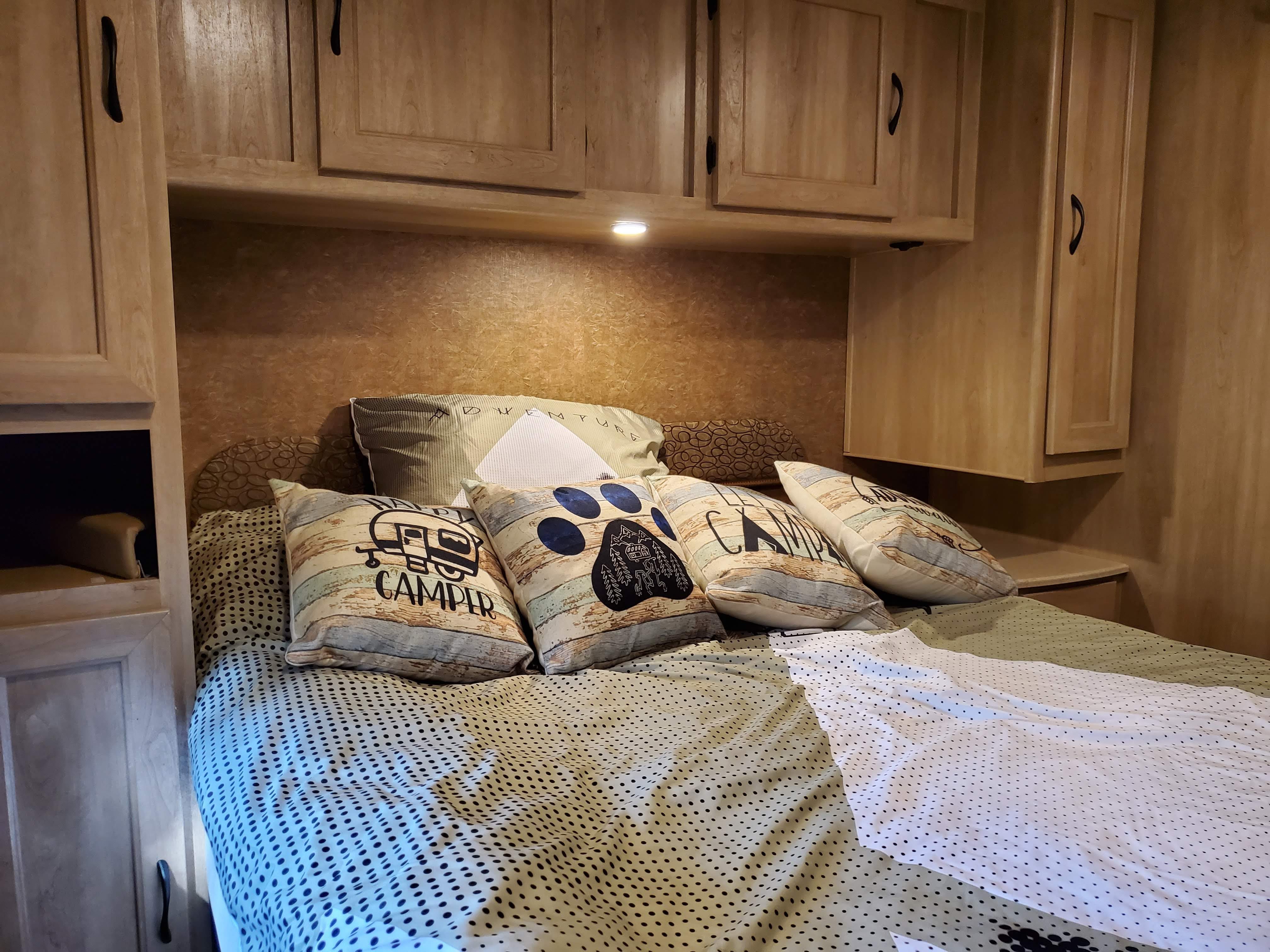 Cozy RV rental bedroom with built-in wooden cabinets, patterned bedding, and fun 'camper' themed pillows.. Forest River Coachmen Freelander 2016
