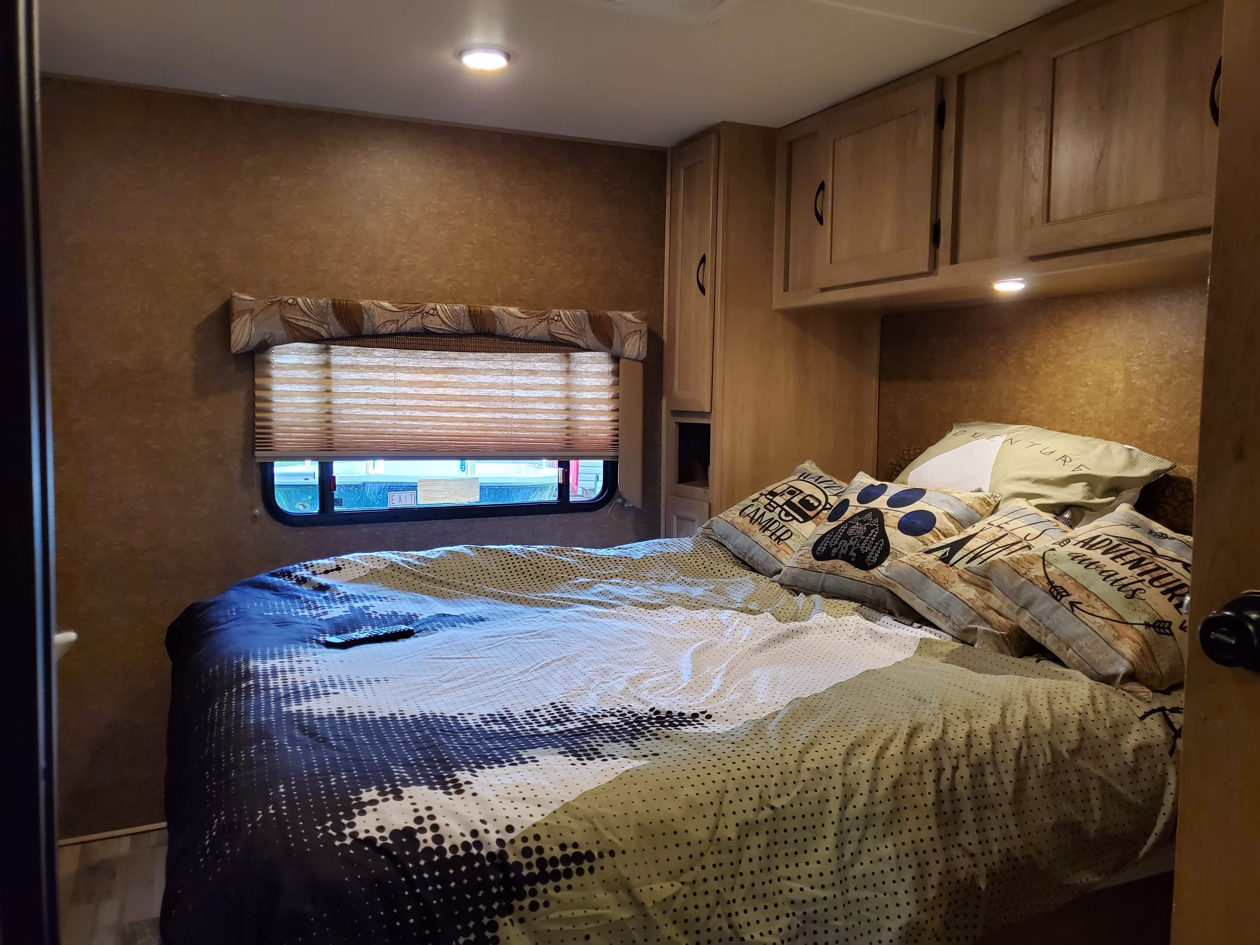 Inside an RV rental, a comfy bedroom setup with a patterned bedspread, decorative pillows, window, and wood cabinetry.. Forest River Coachmen Freelander 2016
