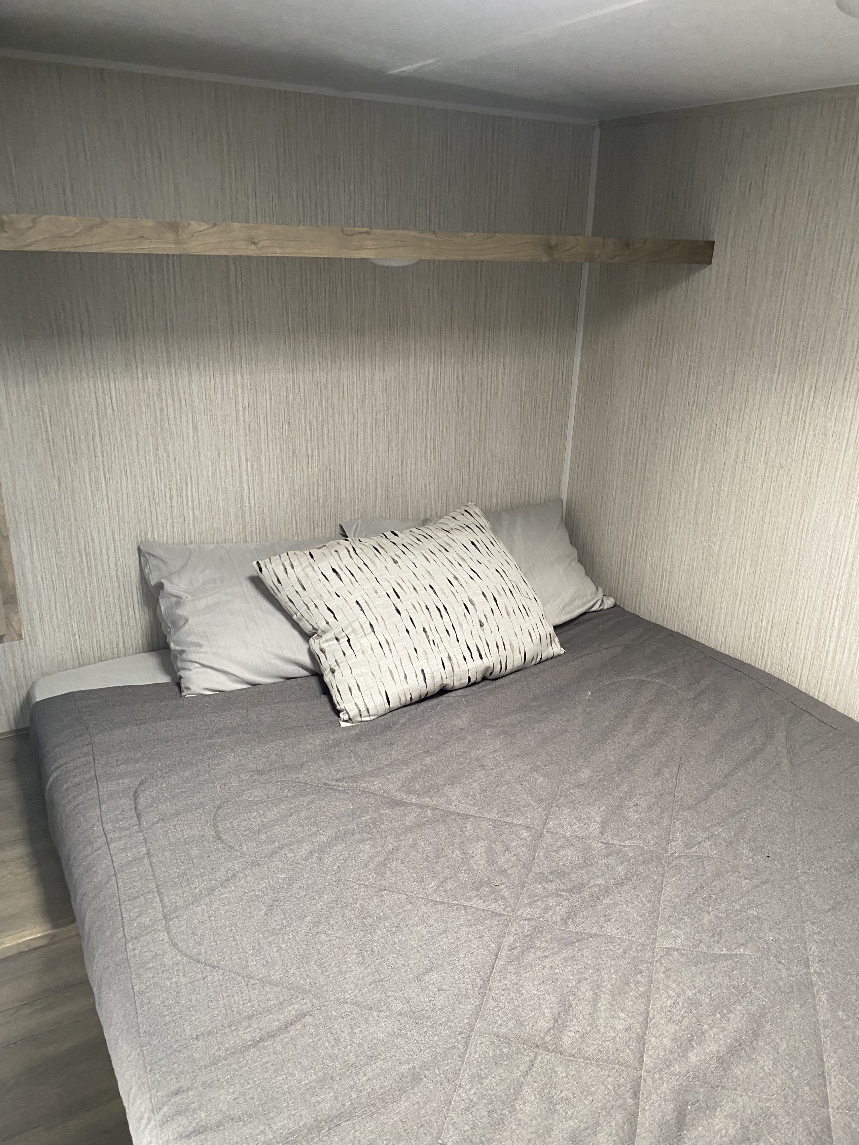 Cozy RV rental bedroom with a comfy grey bed, pillows, and a wooden overhead shelf, perfect for rest.. Forest River Puma 2022