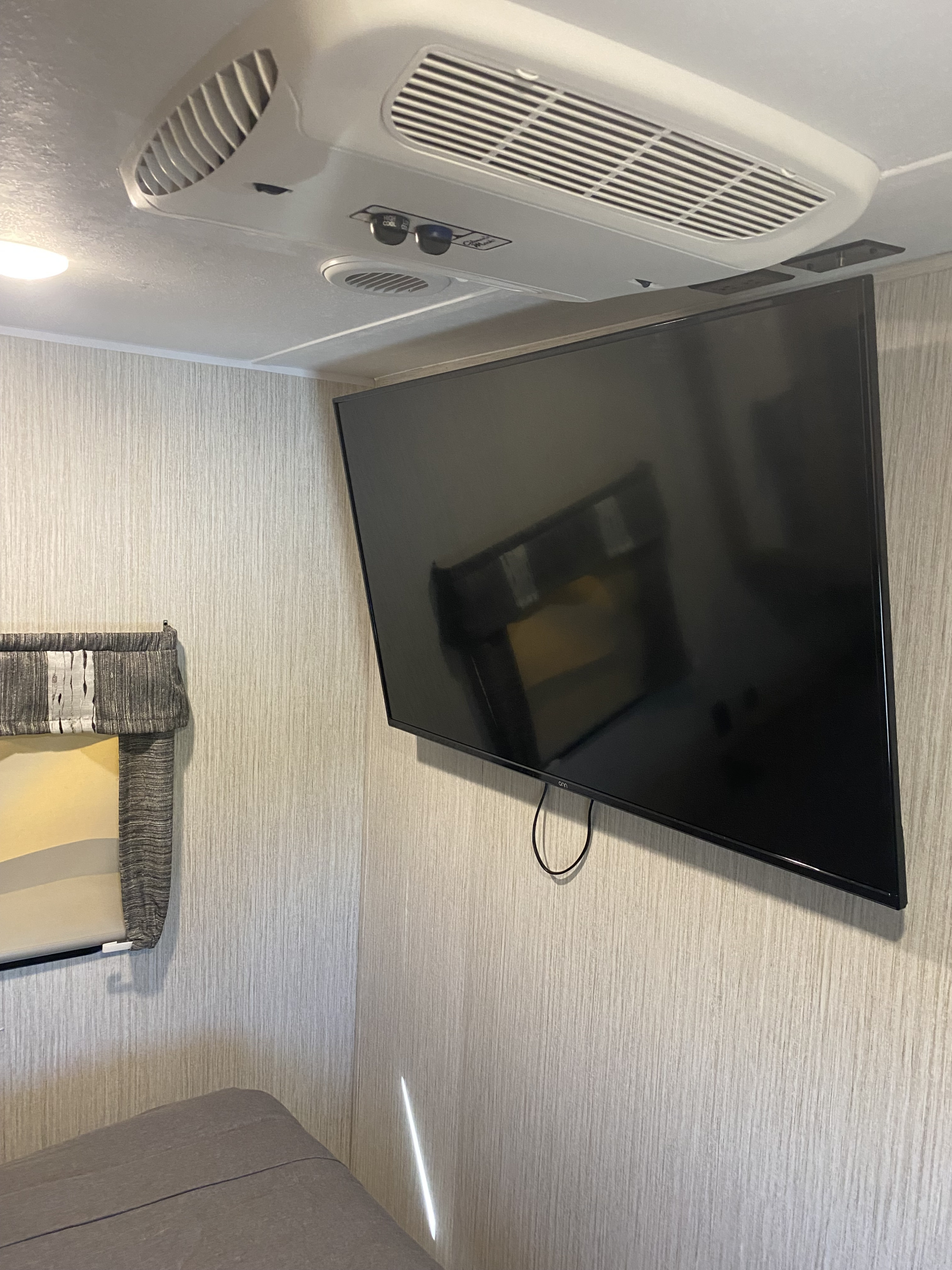 Interior of an RV rental showing an overhead AC unit, wall-mounted TV, and textured walls.. Forest River Puma 2022