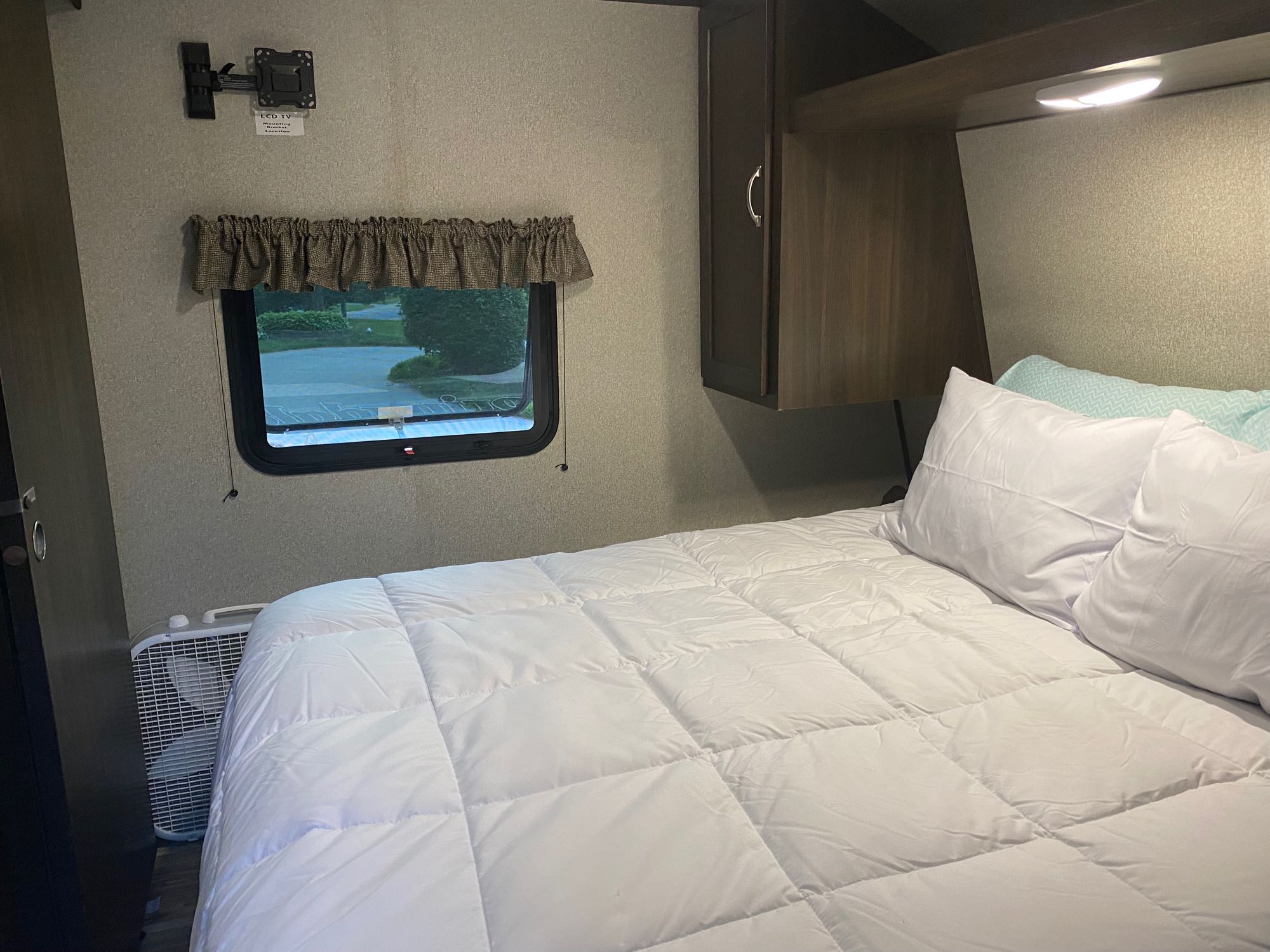 Inside an RV rental: a comfortable bedroom featuring a queen bed, window, and storage cabinets. Ready for your adventure.. Keystone RV Hideout 2023