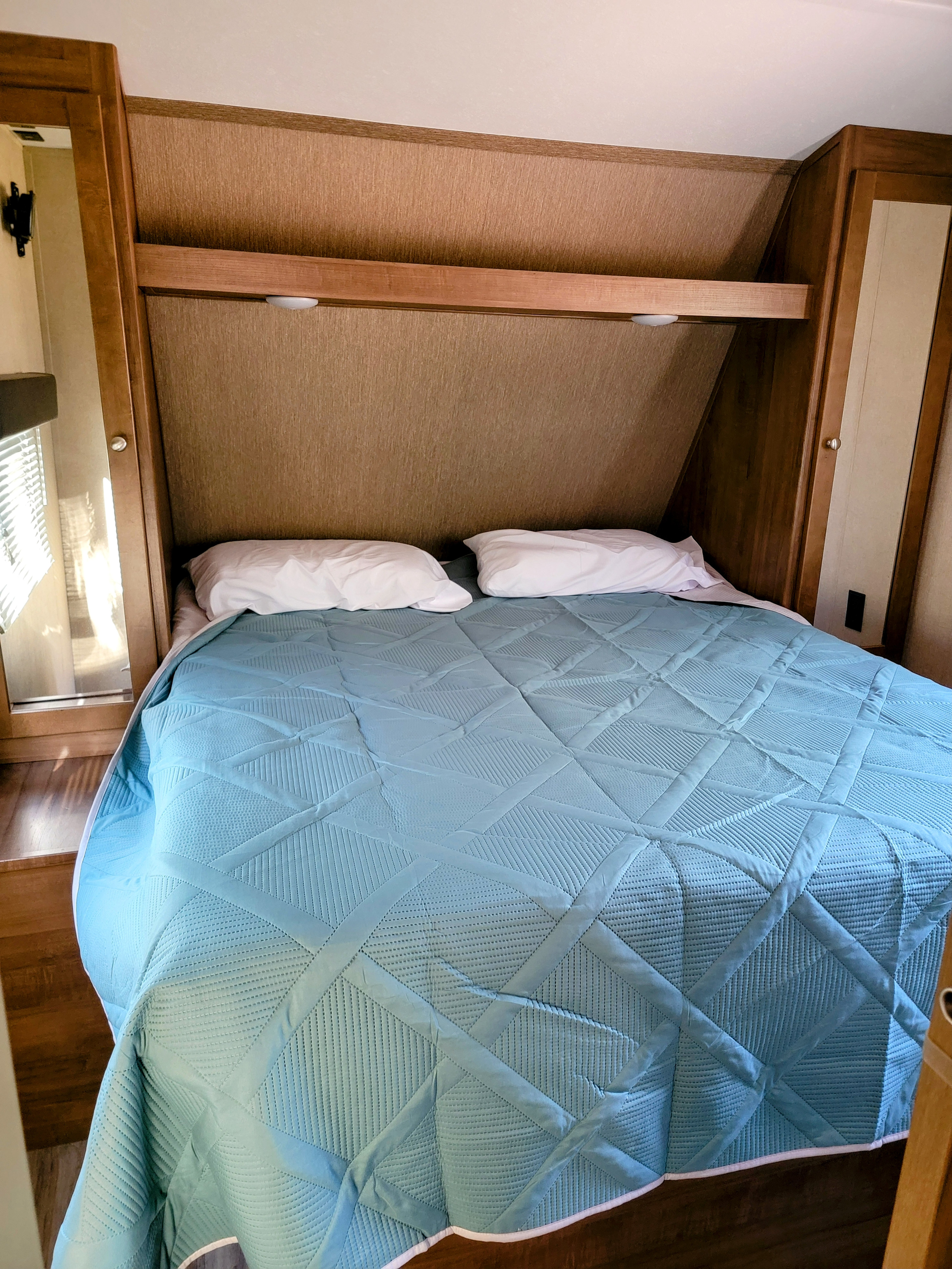Inside a compact RV rental bedroom, featuring a neatly made bed with a blue quilted bedspread & white pillows.. Aspen Trail Aspen Trail Trailer 2018
