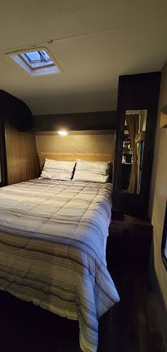 Comfortable RV rental bedroom featuring a full-size bed, skylight, and bedside mirror.. Pacific Coachworks Panther Xtralite 2019