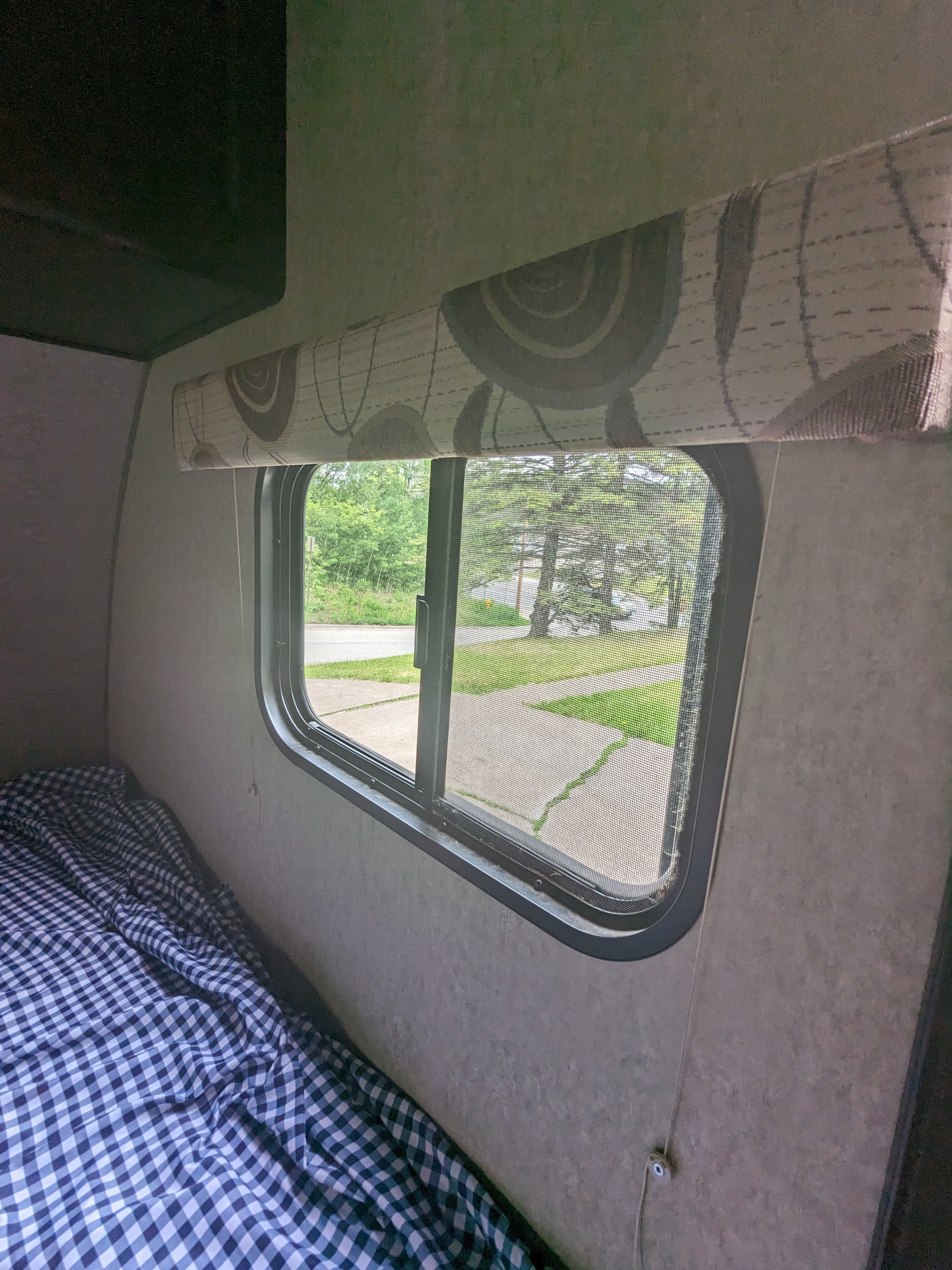 Cozy RV rental interior: checked bed, window with screen view of road & trees.. Forest River Cherokee Wolf Pup 2016