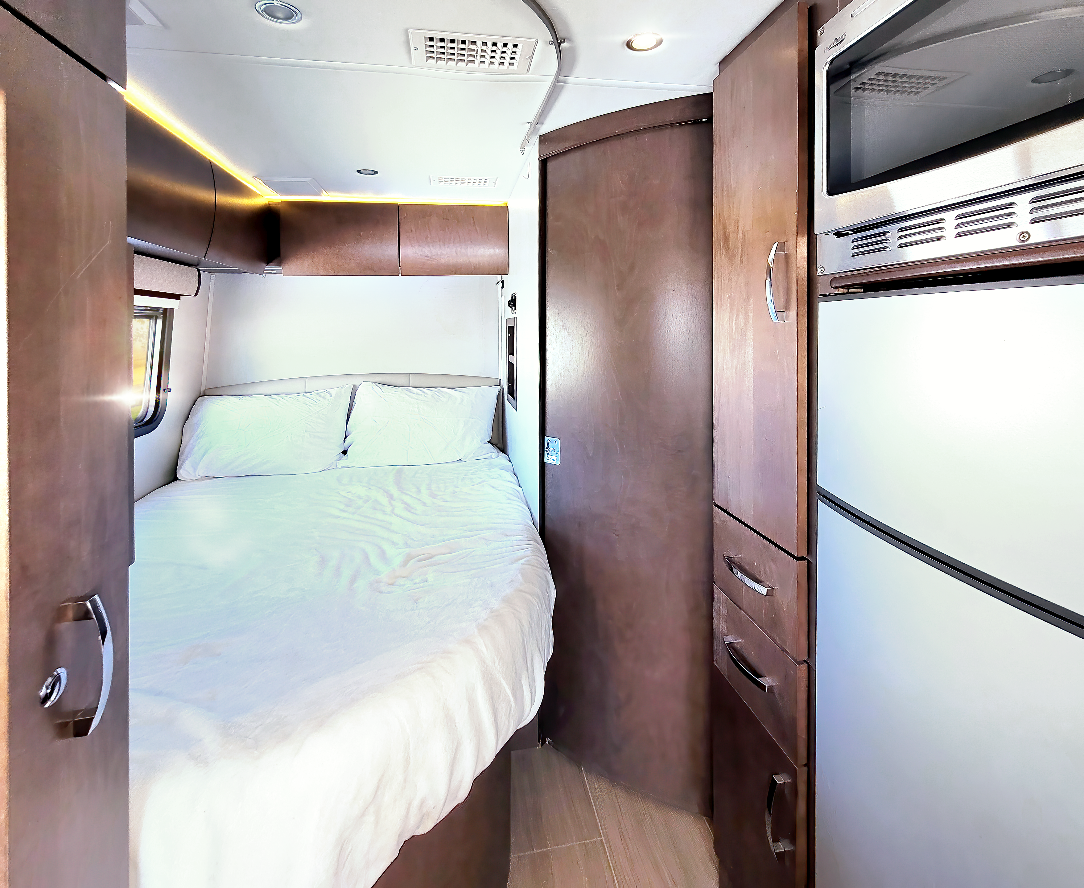 Comfortable RV rental interior featuring a cozy sleeping area, overhead lighting, microwave, and refrigerator.. Leisure Travel Unity 2018