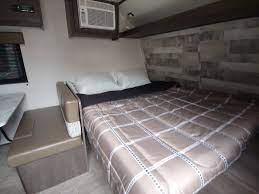 Inside an RV rental: a comfortable bed setup with plaid comforter, side bench seating, and an AC unit for your next trip.. Dutchmen Coleman Lantern LT 2020