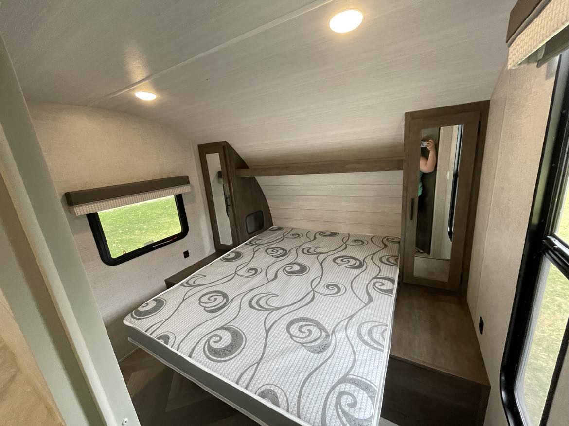Clean RV rental bedroom: queen bed with patterned mattress, window, and mirrored wardrobe for your travels.. Forest River Wildwood X-Lite 2021