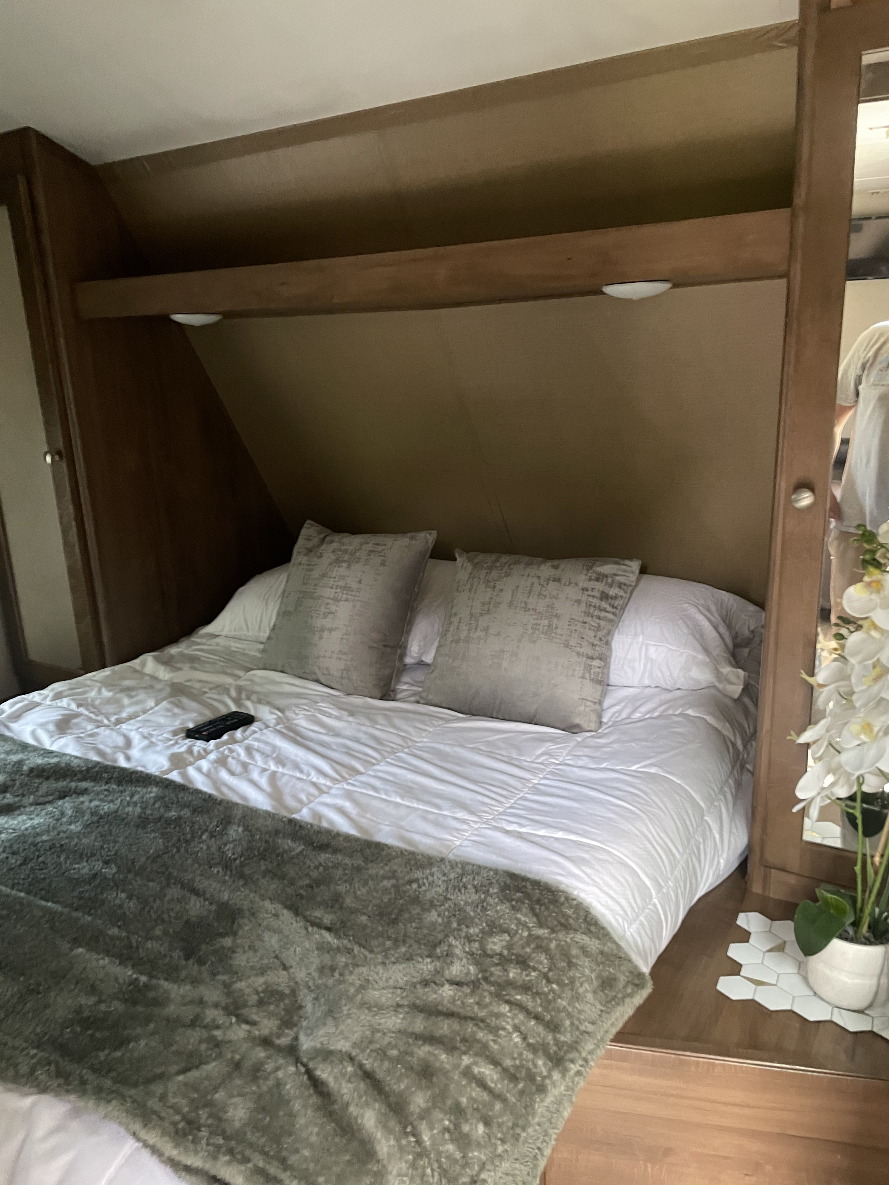 This RV rental offers a compact, comfortable bedroom with a neatly made bed, inviting pillows, and lighting for a restful stay.. Aspen Trail Aspen Trail Trailer 2016