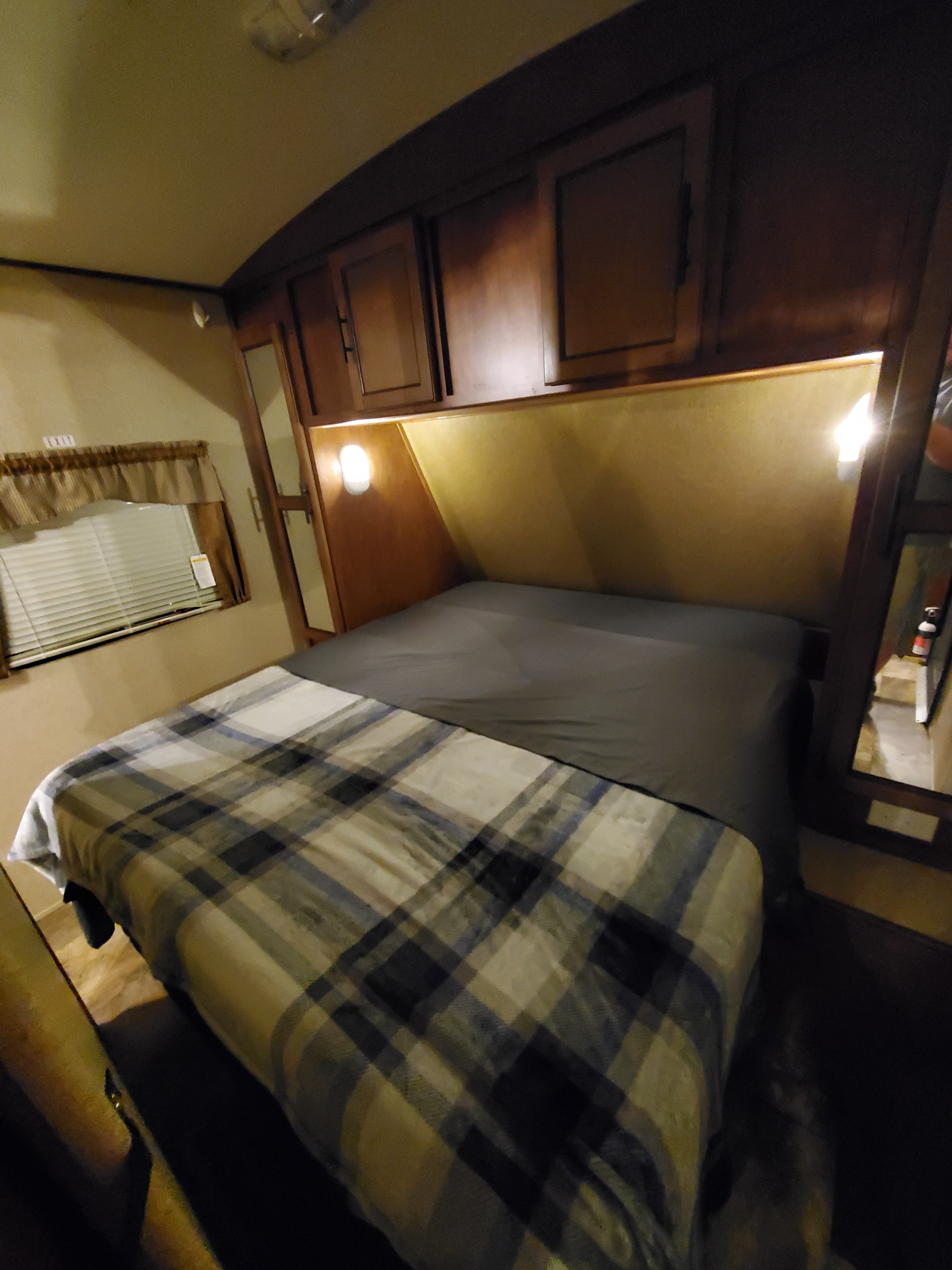 Inside an RV rental, a comfortable bedroom with plaid blanket, overhead cabinets, and a full-length mirror.. Forest River Surveyor 2015