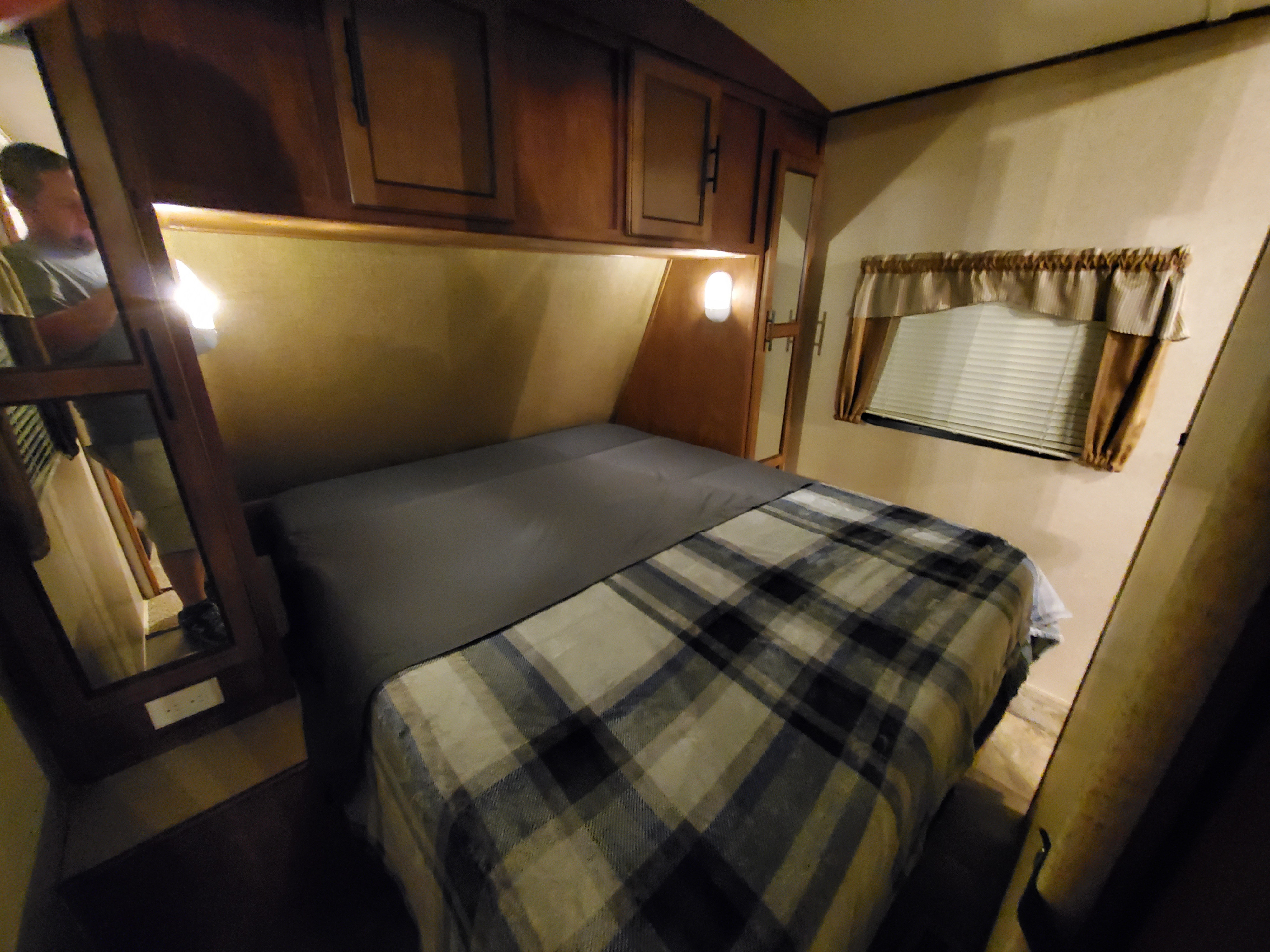 RV rental bedroom featuring a comfy bed with plaid blanket, overhead cabinets, and window. A compact travel space.. Forest River Surveyor 2015