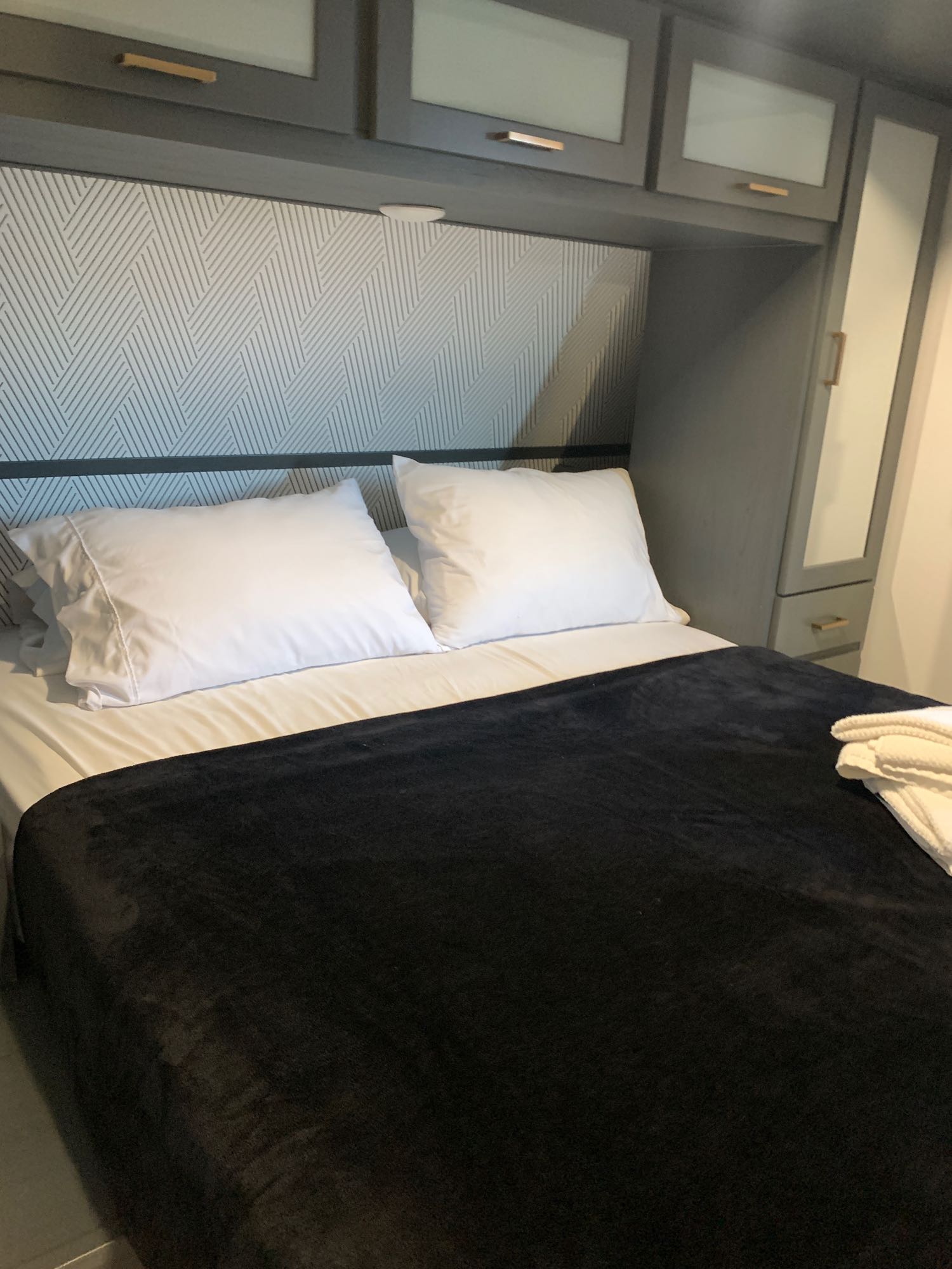 Compact RV rental bedroom with white pillows, black blanket, patterned headboard & overhead storage.. Keystone RV Bullet Ultra Lite 2022