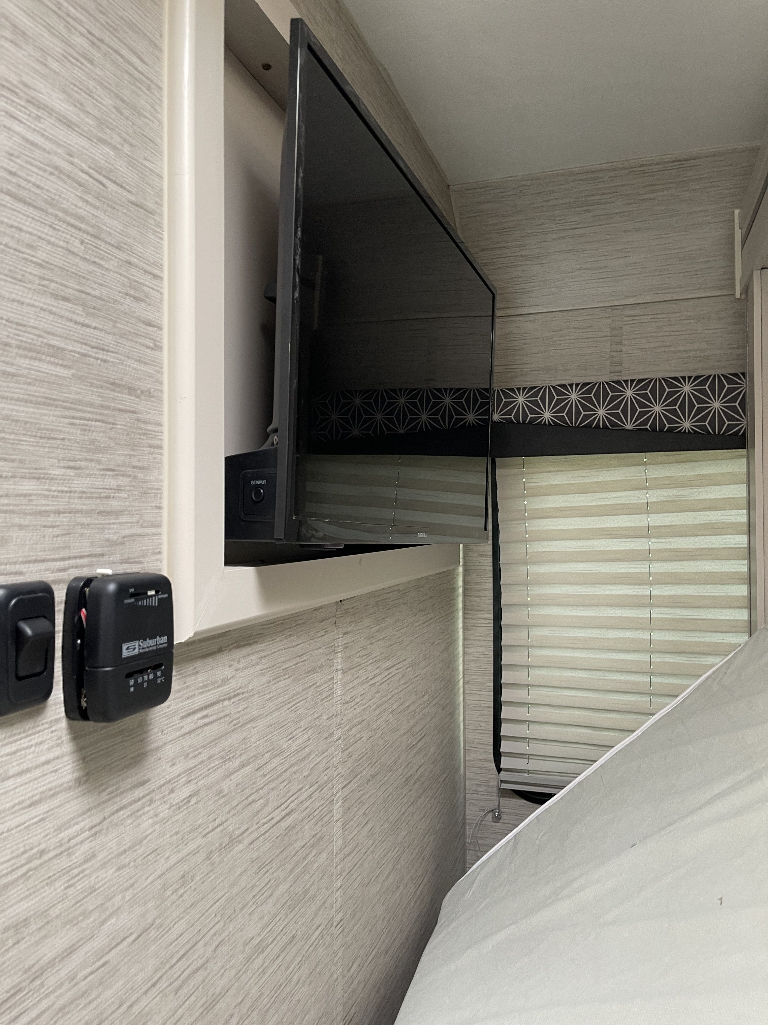 RV rental interior shows a wall-mounted TV, Suburban thermostat, and pleated window blinds in a light-colored bedroom.. Thor Freedom Elite 2022
