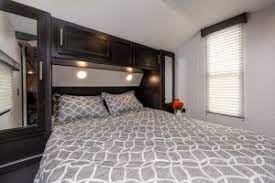Comfortable RV rental bedroom with patterned bedding, built-in storage, and window for cozy travel accommodation.. Forest River Cherokee Grey Wolf 2021