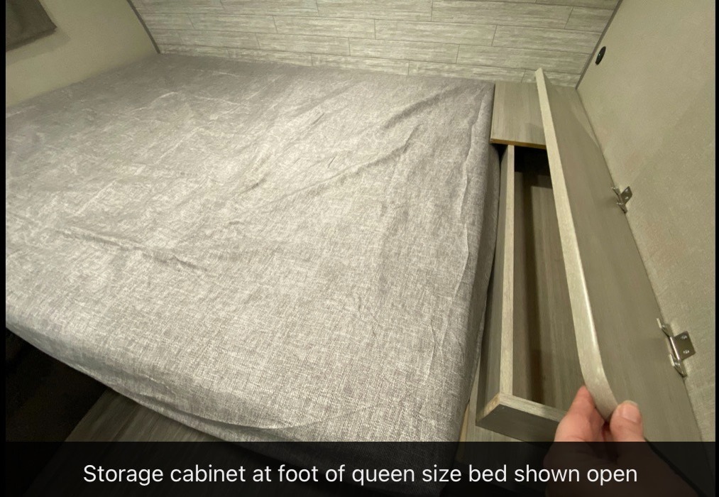 RV rental interior: Queen bed (grey sheets) next to an open, light wood storage cabinet, revealing a compartment.. Forest River Aurora Lite 16BHX 2023