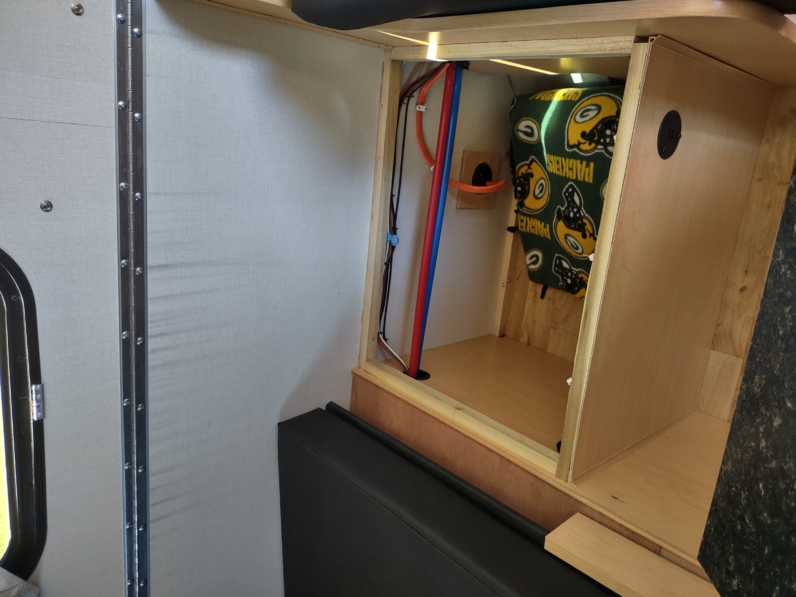 RV rental interior: A compact space with black seating, exposed plumbing, wiring, and a Packers blanket in storage.. A Liner A Liner Popup Trailer 2022