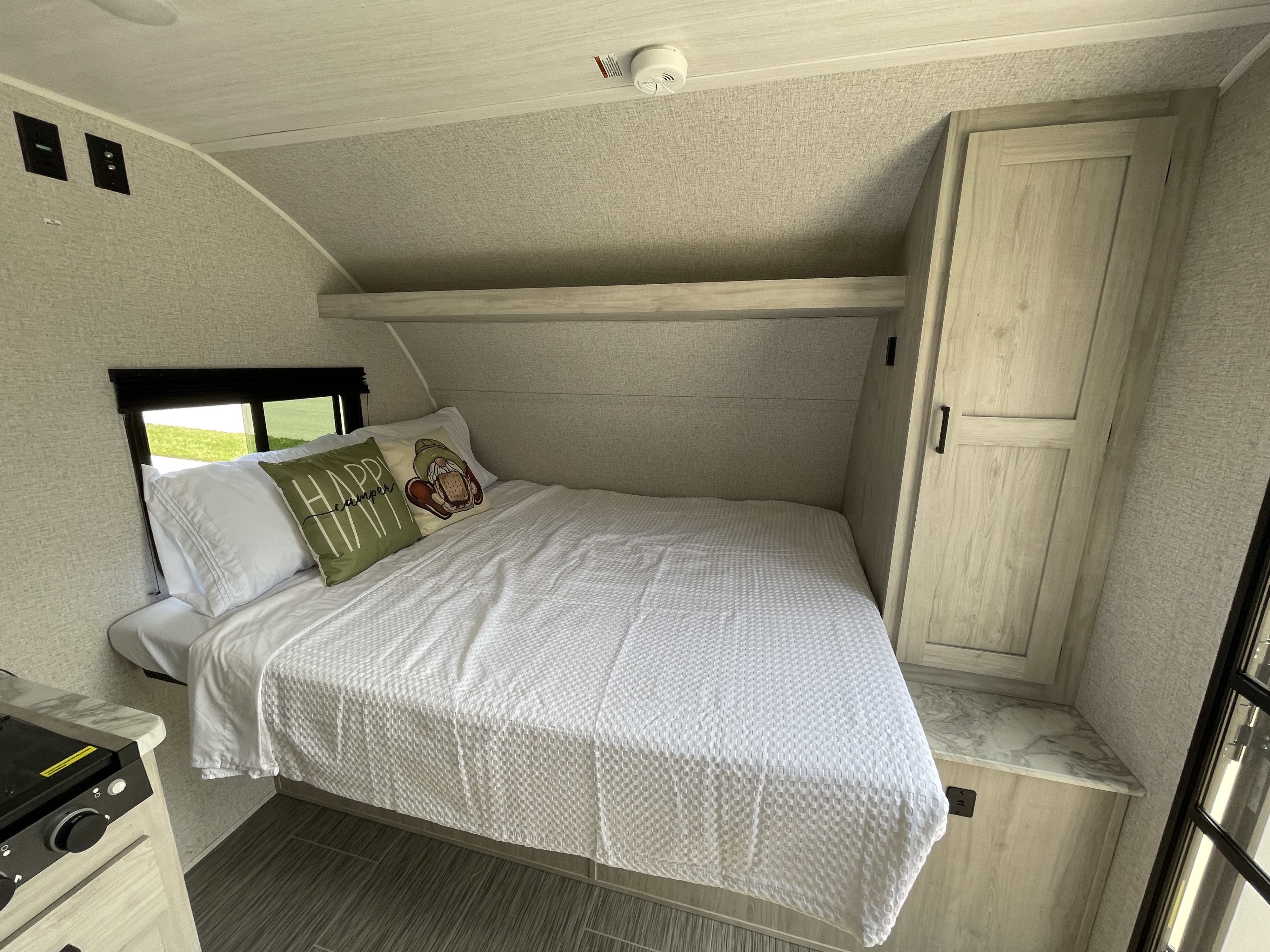 This RV rental bedroom features a comfy bed, window view, and compact storage, showcasing a functional camper interior.. East to West Silver Lake LE 2023