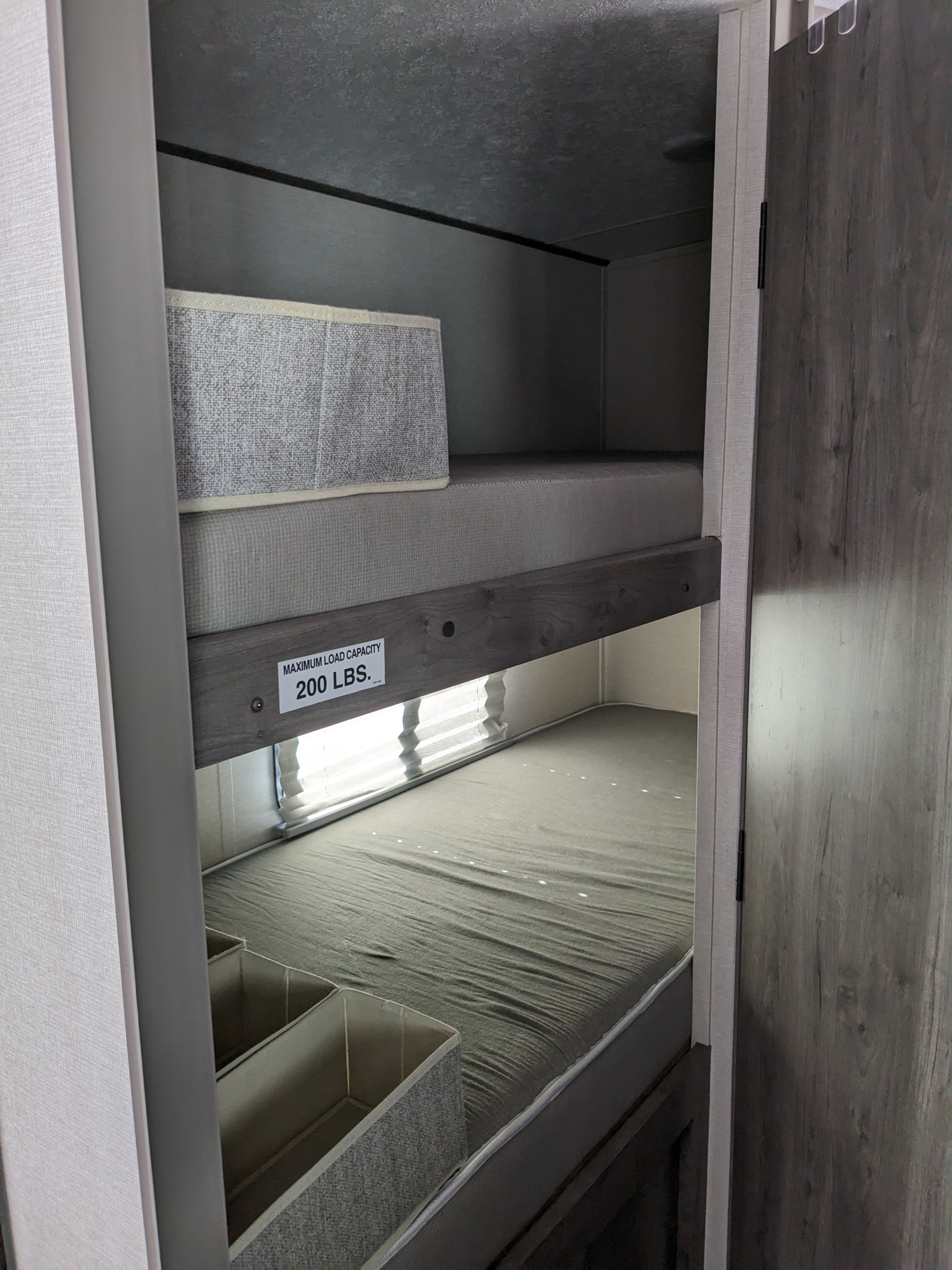 Interior of an RV rental: detailed view of comfortable bunk beds, with the top bunk labeled for a 200 lbs max load.. Coachmen Apex Nano 2021