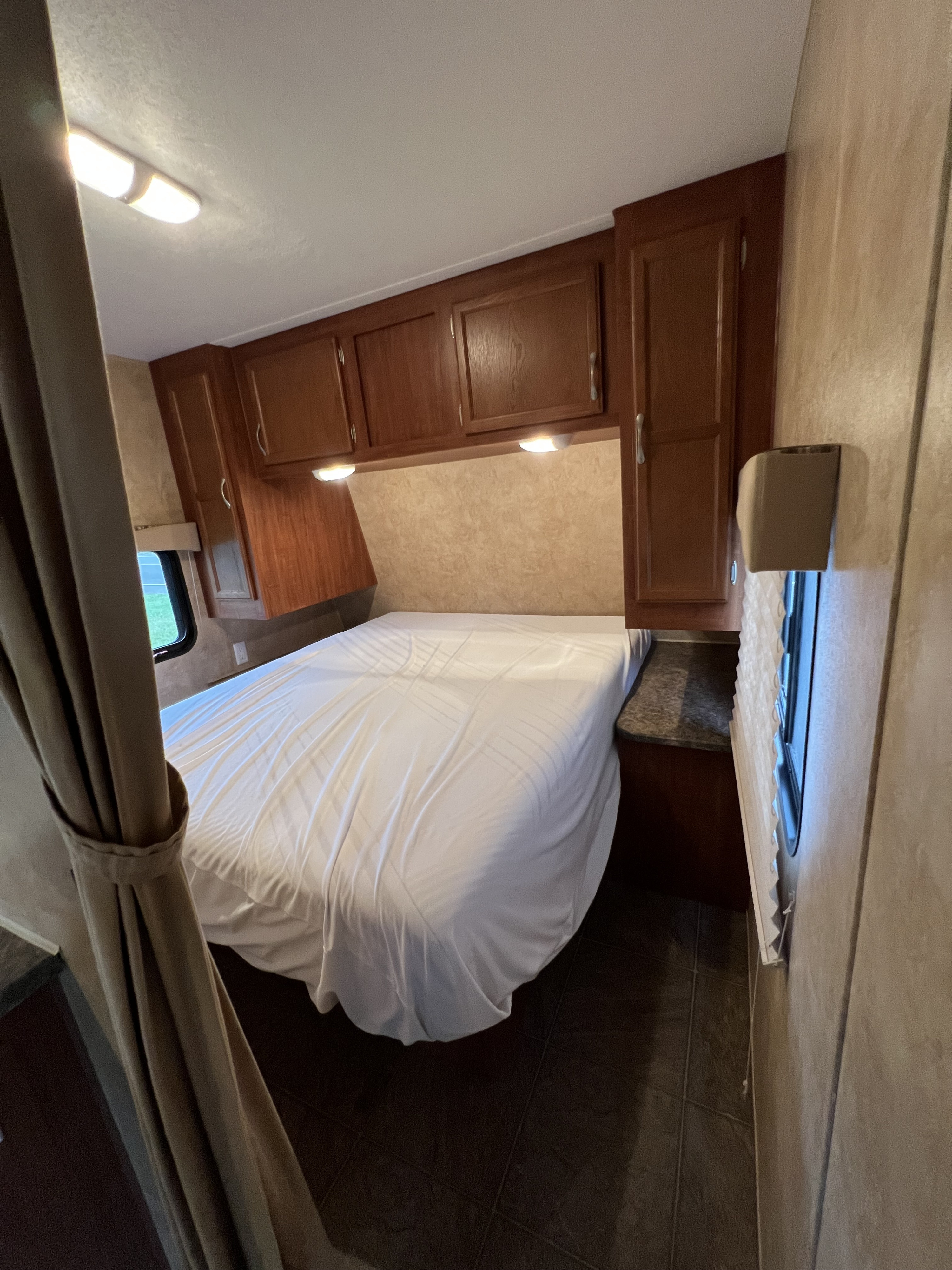 RV rental: cozy bedroom featuring a neatly made white bed, wood cabinets, and task lighting. Ready for travel.. Jayco Jay Flight 2011