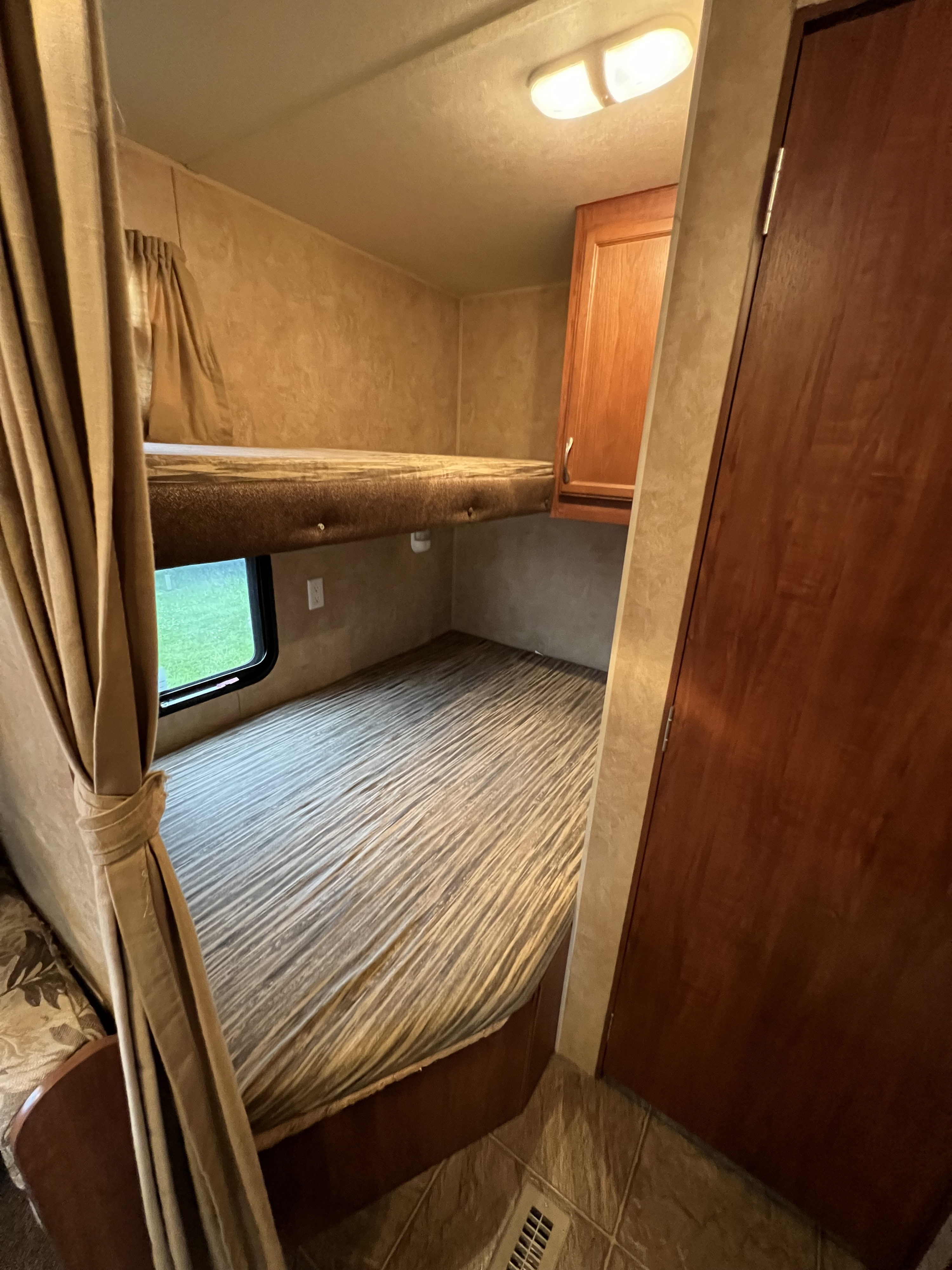 Inside an RV rental: a cozy bunk bed sleeping area with window, curtains, and storage, ideal for compact travel.. Jayco Jay Flight 2011