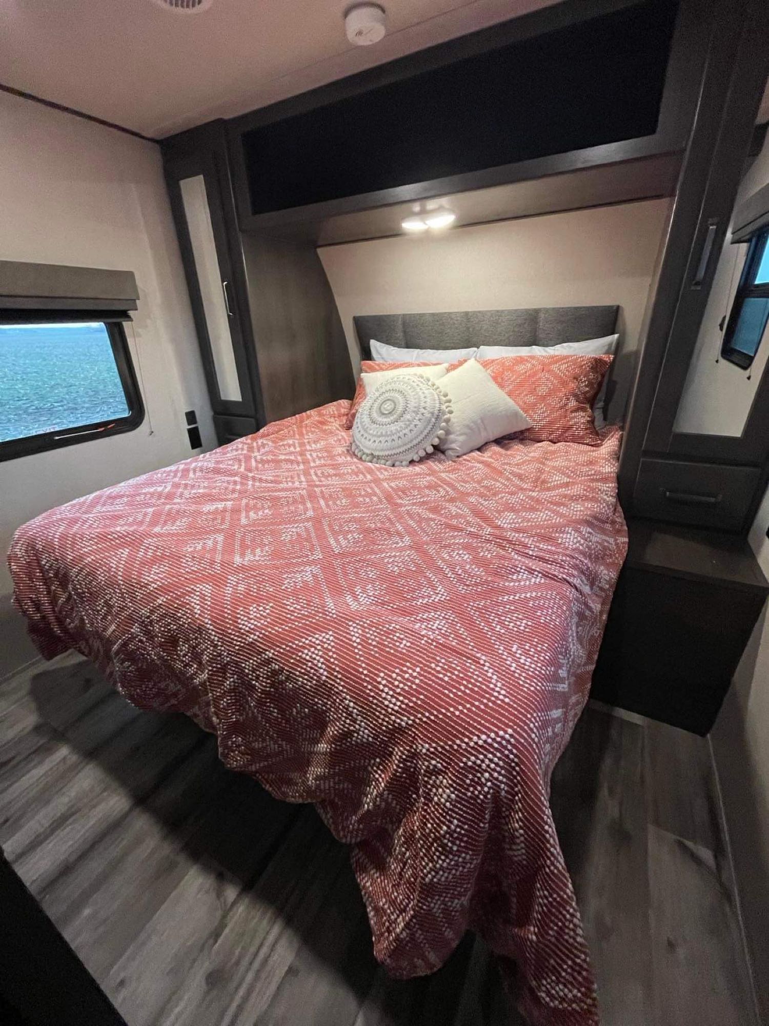 Comfortable RV rental bedroom featuring patterned bedding, modern built-ins, and a beautiful water view.. Grand Design Transcend Xplor 2023