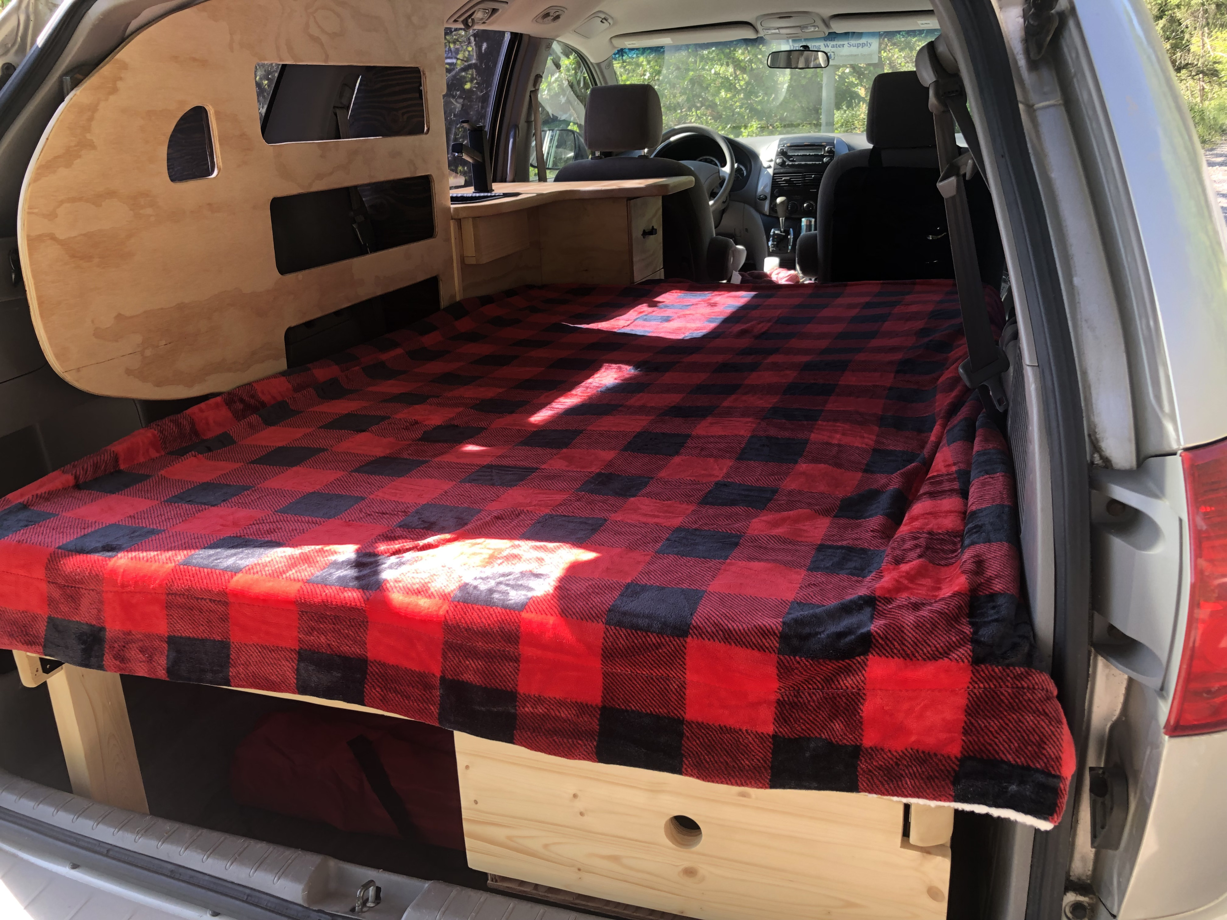 A cozy minivan bed setup with storage and a small counter, ideal for an RV rental camping trip.. Toyota Hiace 2007