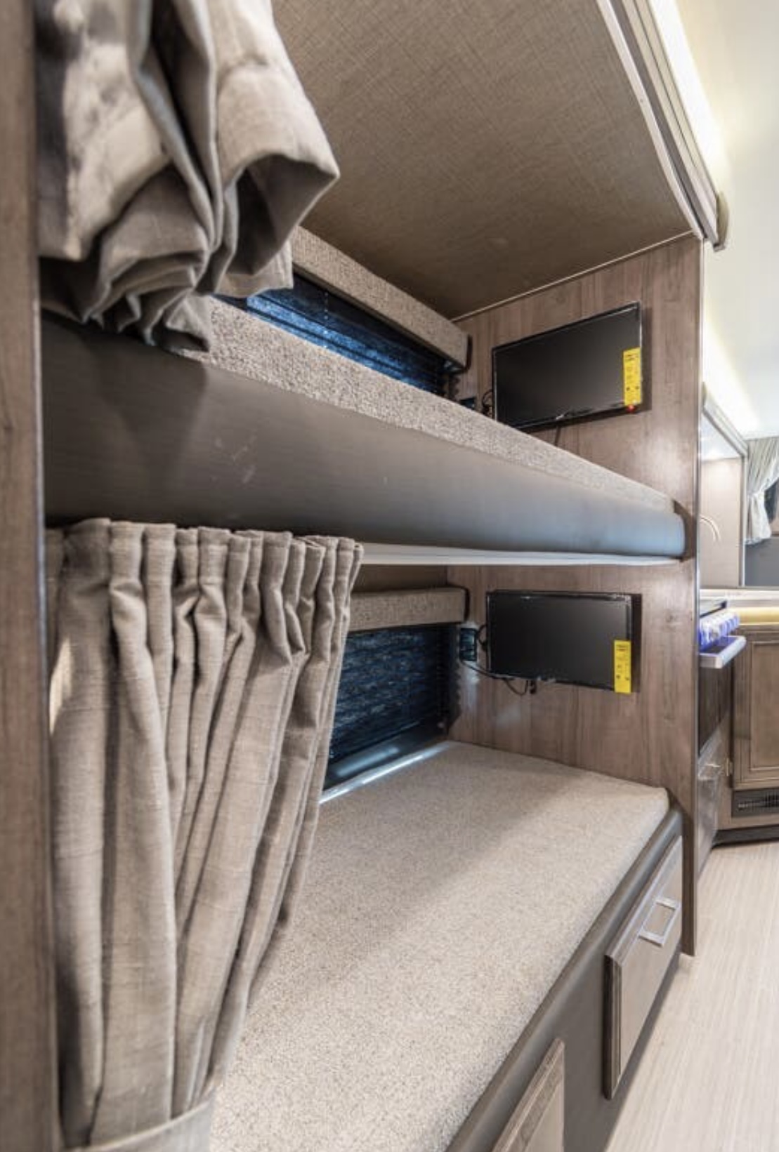 RV rental bunk beds featuring individual TVs and privacy curtains, offering cozy sleeping space for travelers.. Entegra Coach Odyssey 2022
