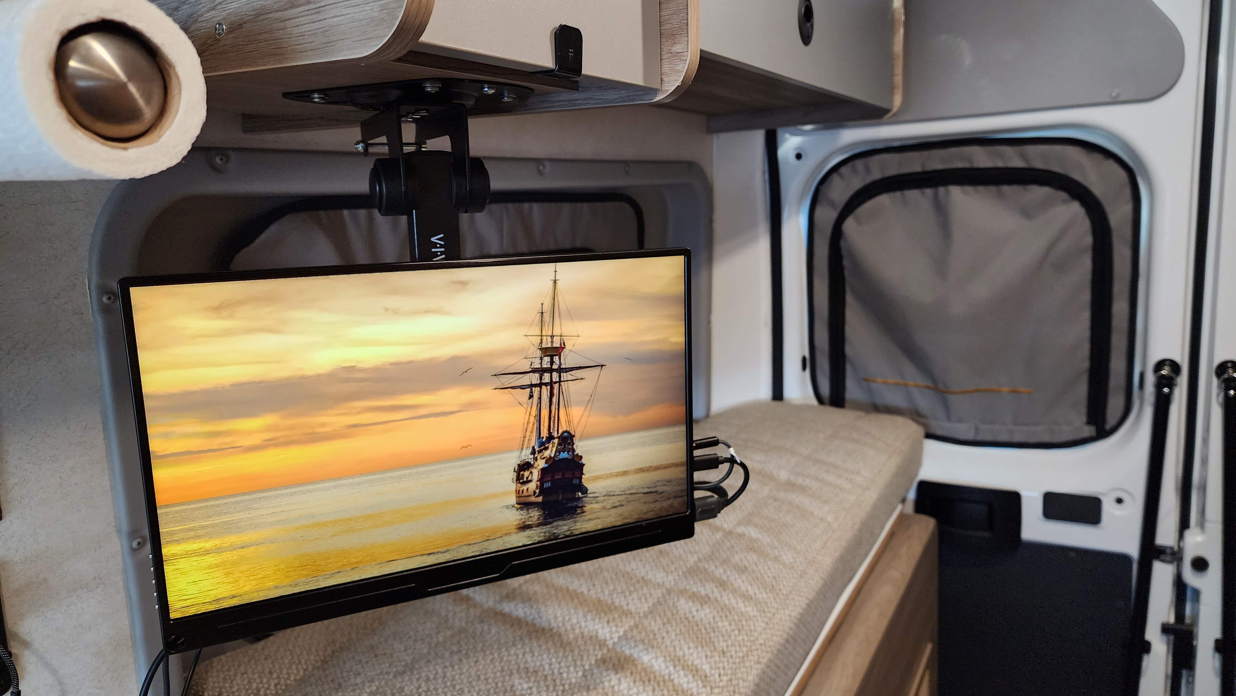 Cozy rv rental interior with ceiling-mounted TV showing a ship on the ocean at sunset, next to a comfortable bench bed.. Winnebago Solis 2023
