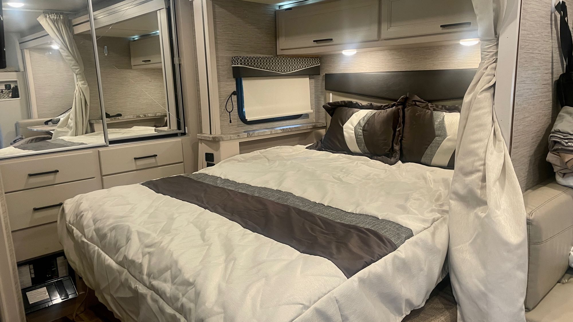 Cozy RV rental bedroom with modern decor, a comfortable bed, mirrored storage, and overhead cabinets.. Thor Compass 2021