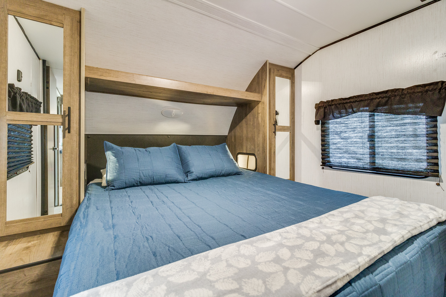 Cozy RV rental bedroom featuring a blue bed, mirrored closet, and window. Ideal for compact living.. Heartland RVs Pioneer 2022