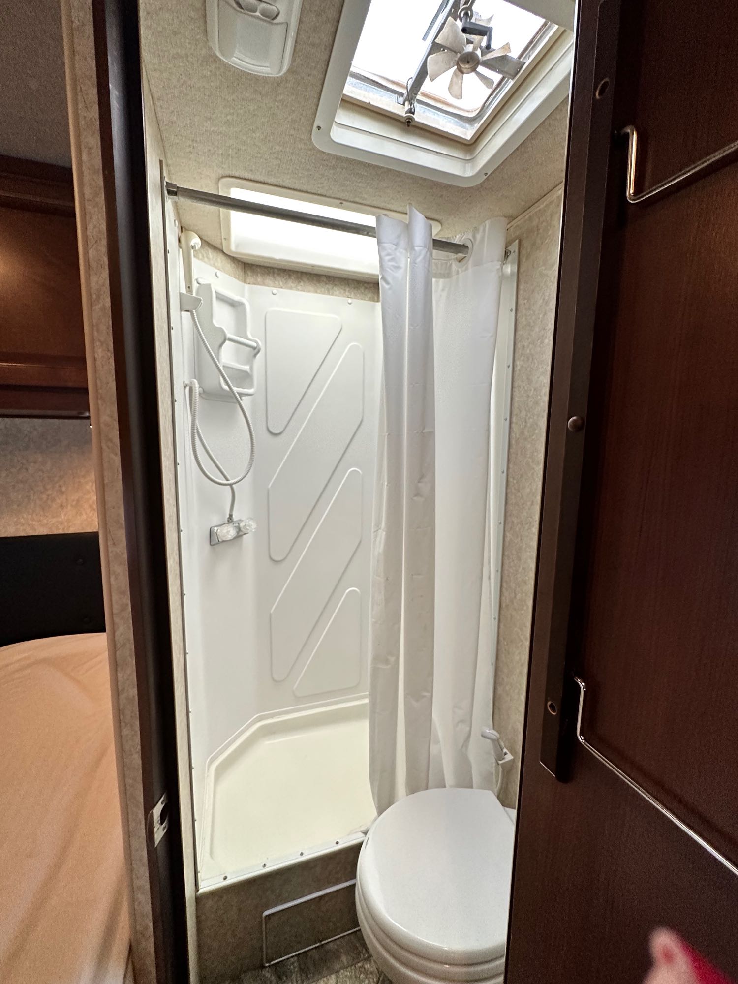 RV rental's compact bathroom features a bright white shower stall, curtain, toilet, and overhead skylight fan.. Jamboree Searcher 2013