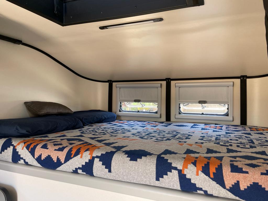 Experience comfort in this RV rental's sleeping loft, featuring a vibrant blanket, pillows, and privacy windows.. Ford F350 2017