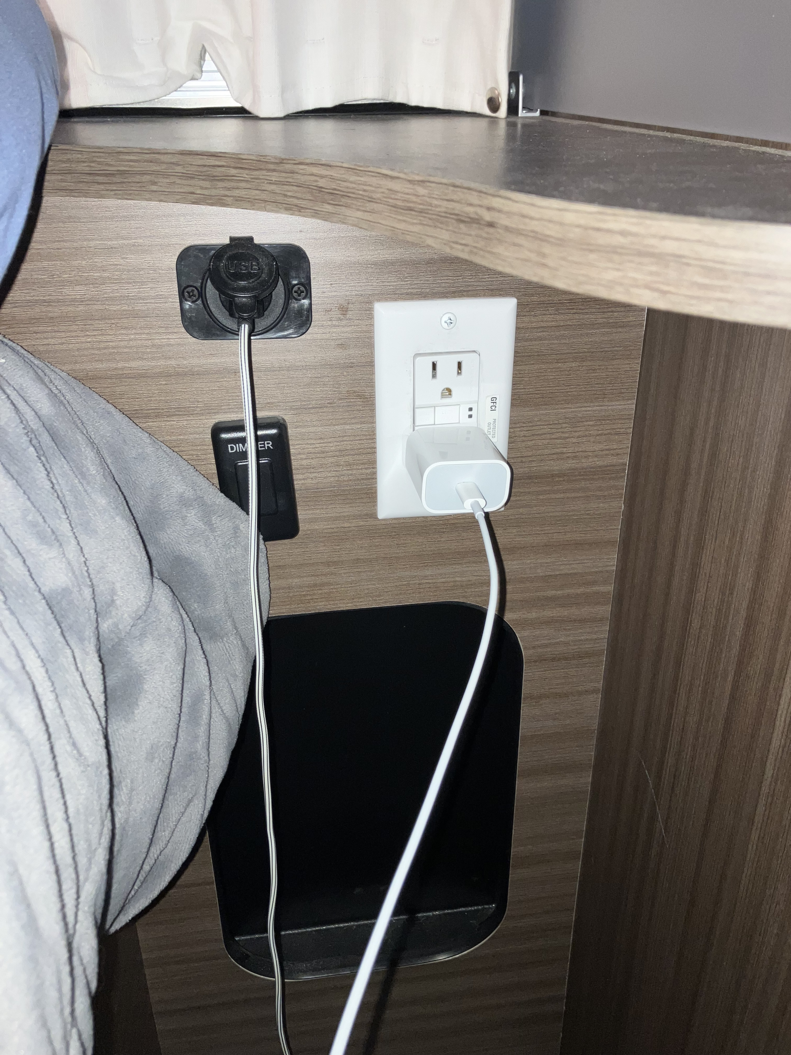 RV rental charging setup: wall-mounted USB, GFCI outlet with adapter, and dimmer switch next to a bed.. Airstream Caravel 2022